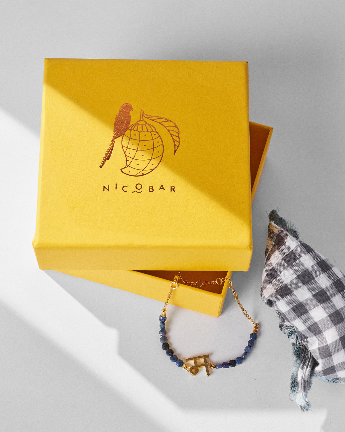 Akshar Bracelet (M) - Gold resting beside a yellow gift box.