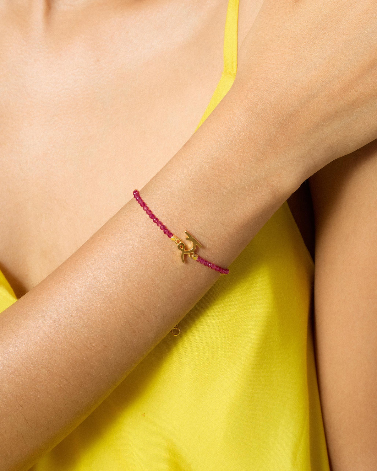 Person wearing Akshar Bracelet (R) - Gold on the forearm with pink beads.