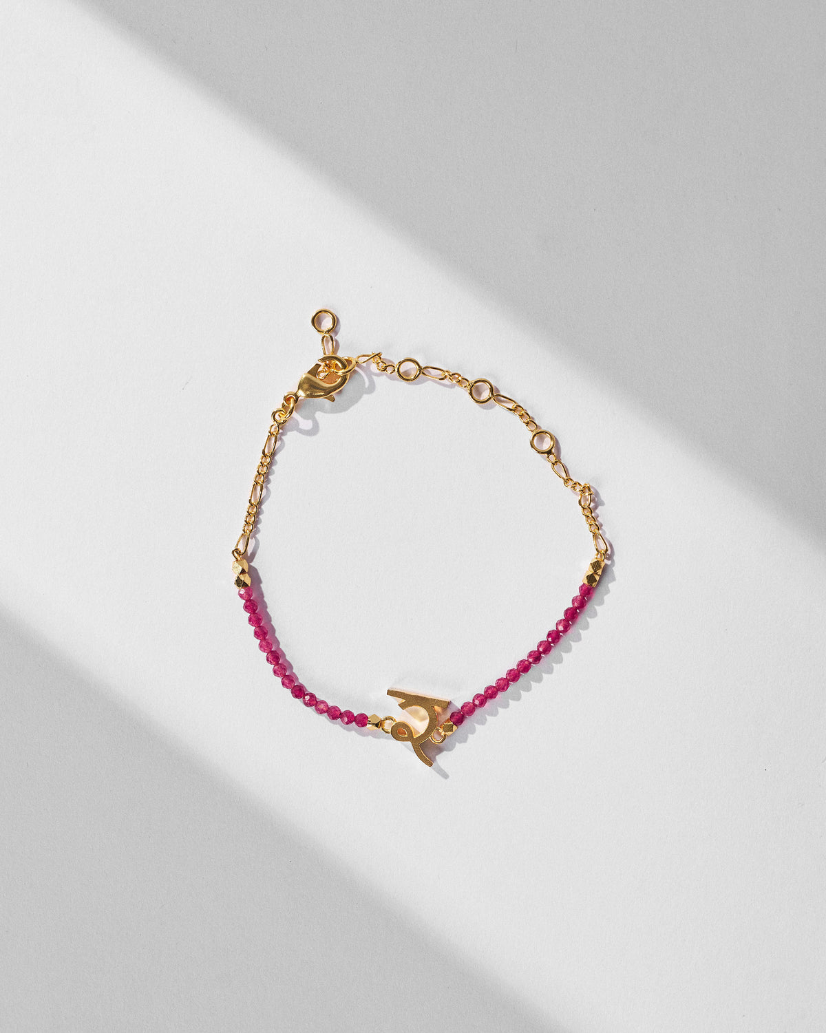 Akshar Bracelet (R) - Gold laid flat, with pink beads and a gold charm.