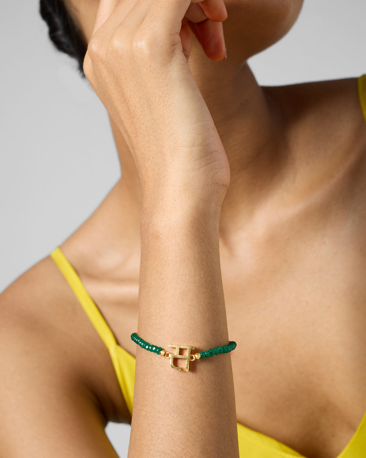 Person wearing Akshar Bracelet (S) - Gold on the wrist, with green beads.