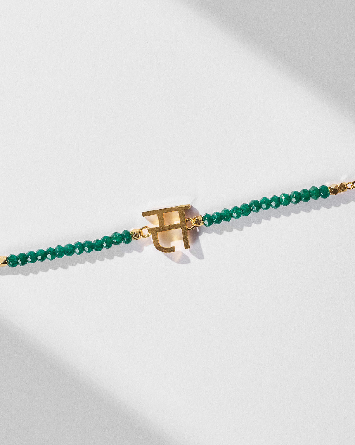 Close-up of Akshar Bracelet (S) - Gold showing its charm and green beads.