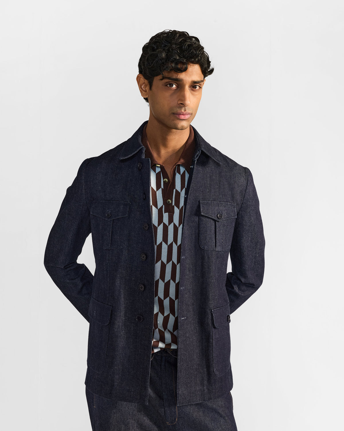 Indigo denim Ibex travel jacket worn open over a patterned polo.