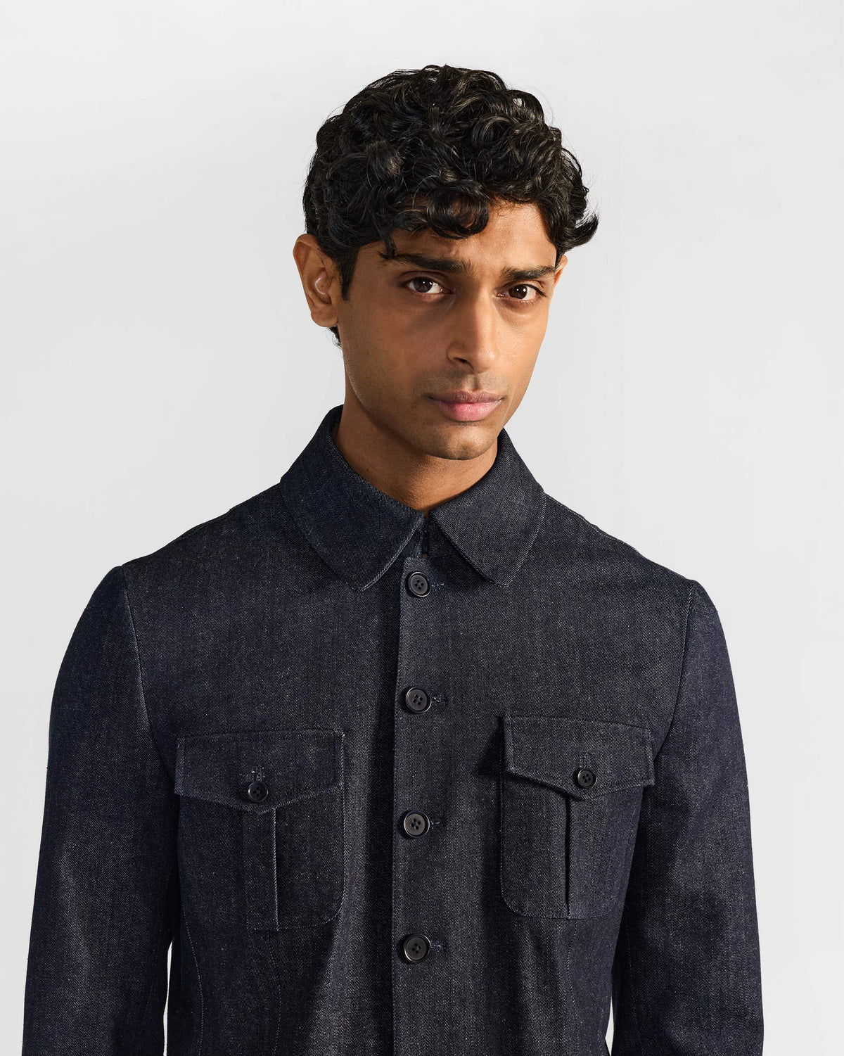 Person wearing an indigo denim Ibex travel jacket with buttoned chest pockets.