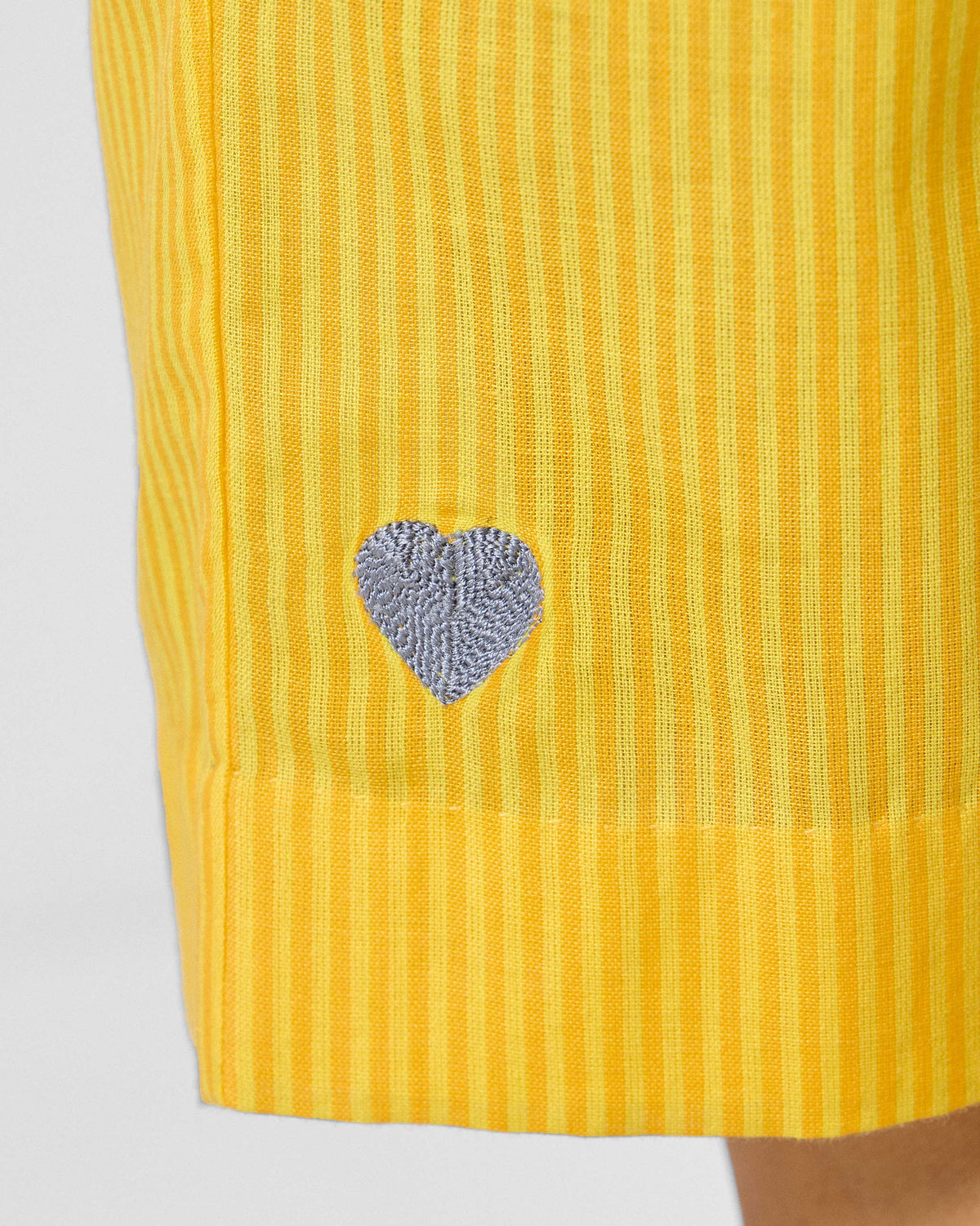 Close-up of a silver heart embroidery on yellow striped Arzoie pants.