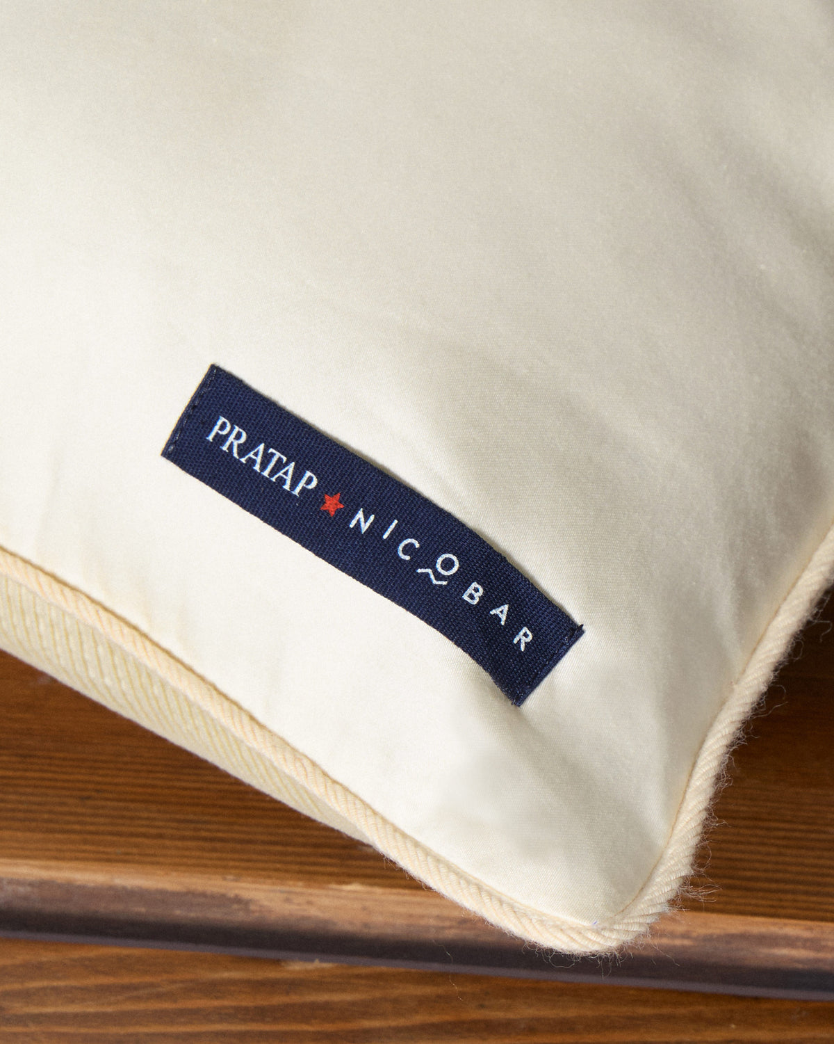 Close-up of the Pratap Nicobar label on the cream Nilgiri cushion cover.