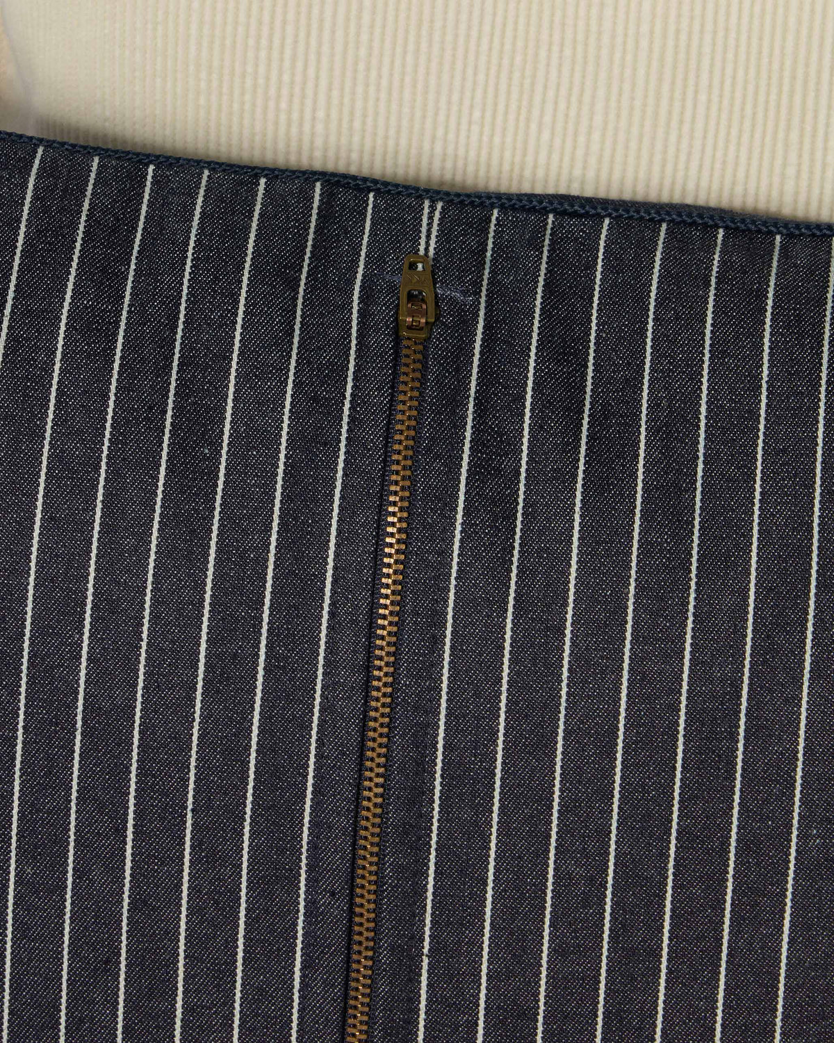Close-up of the brass zip on the back of a navy pinstriped Mistflower cushion.