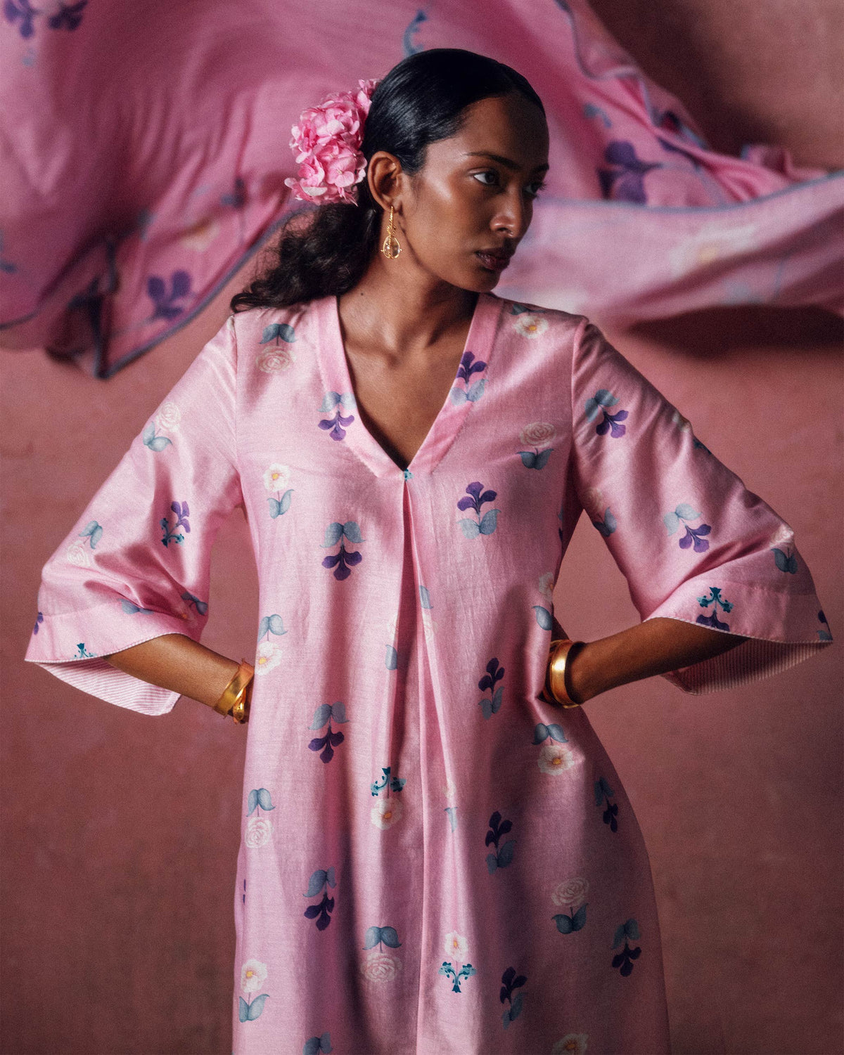 Person wearing a soft pink floral Hera Kurta with a center pleat at the V-neck.