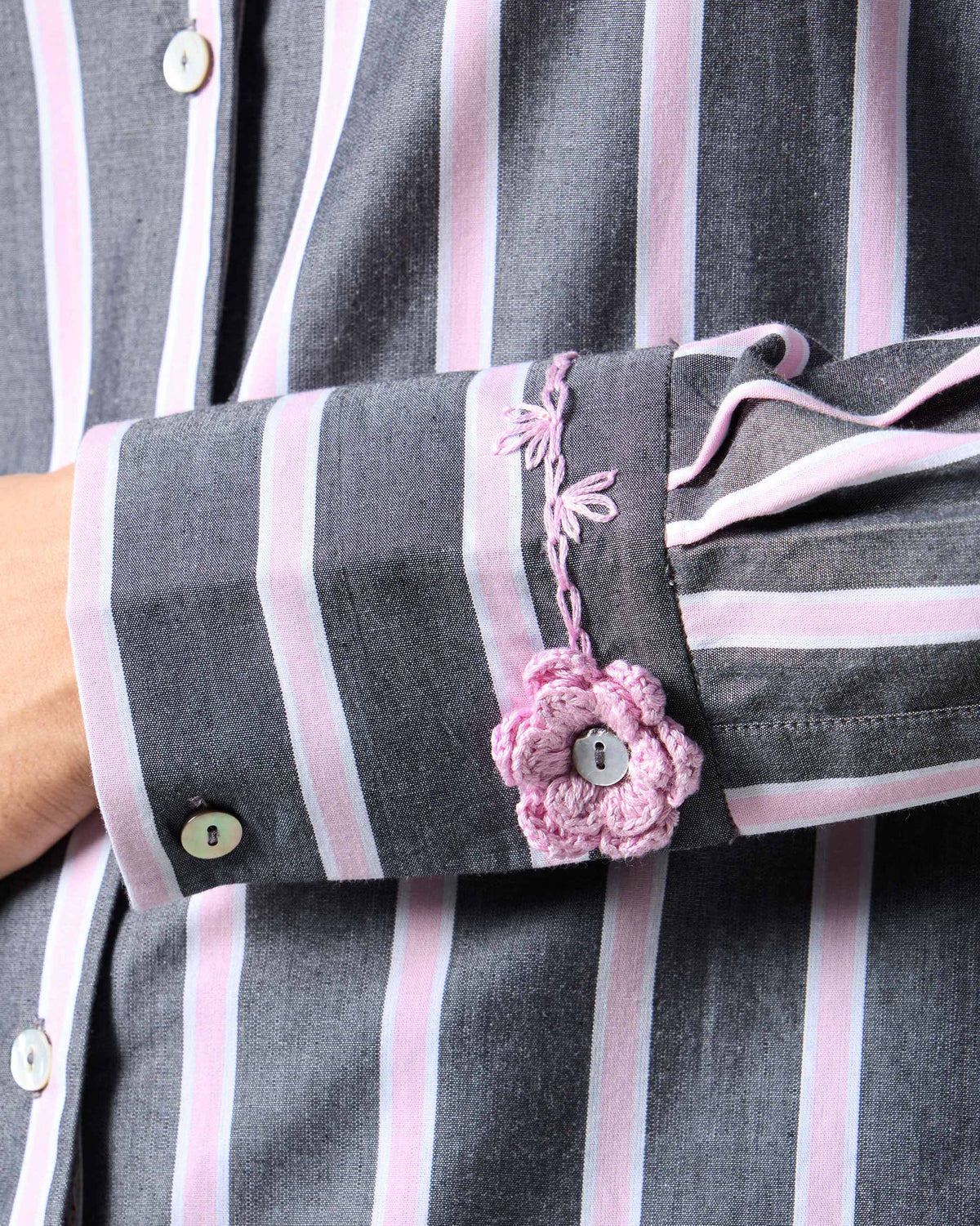 Close-up of a pink crochet flower on the cuff of a striped Trench shirt.