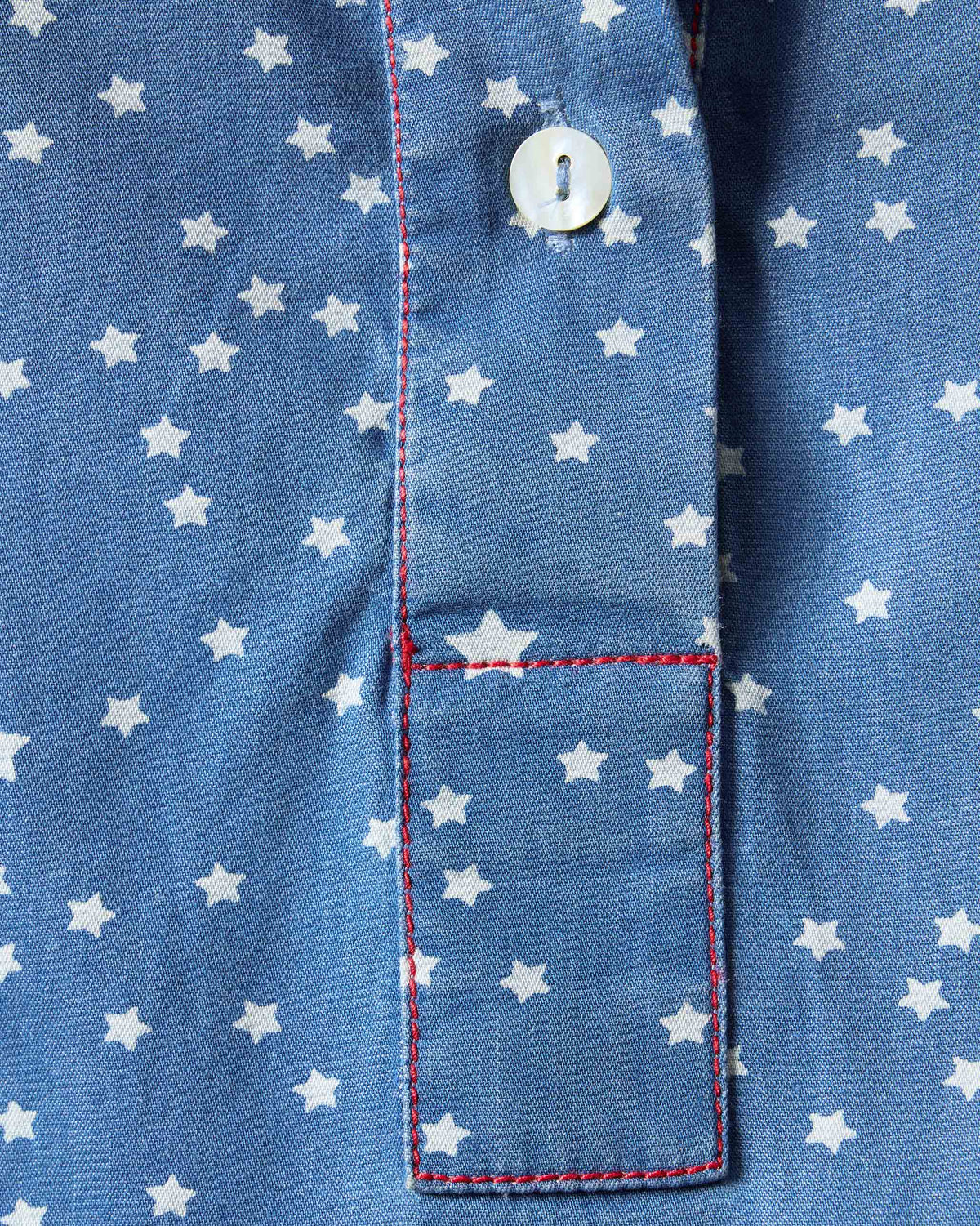 Close-up of a blue Swing top showing red contrast stitching on the placket.