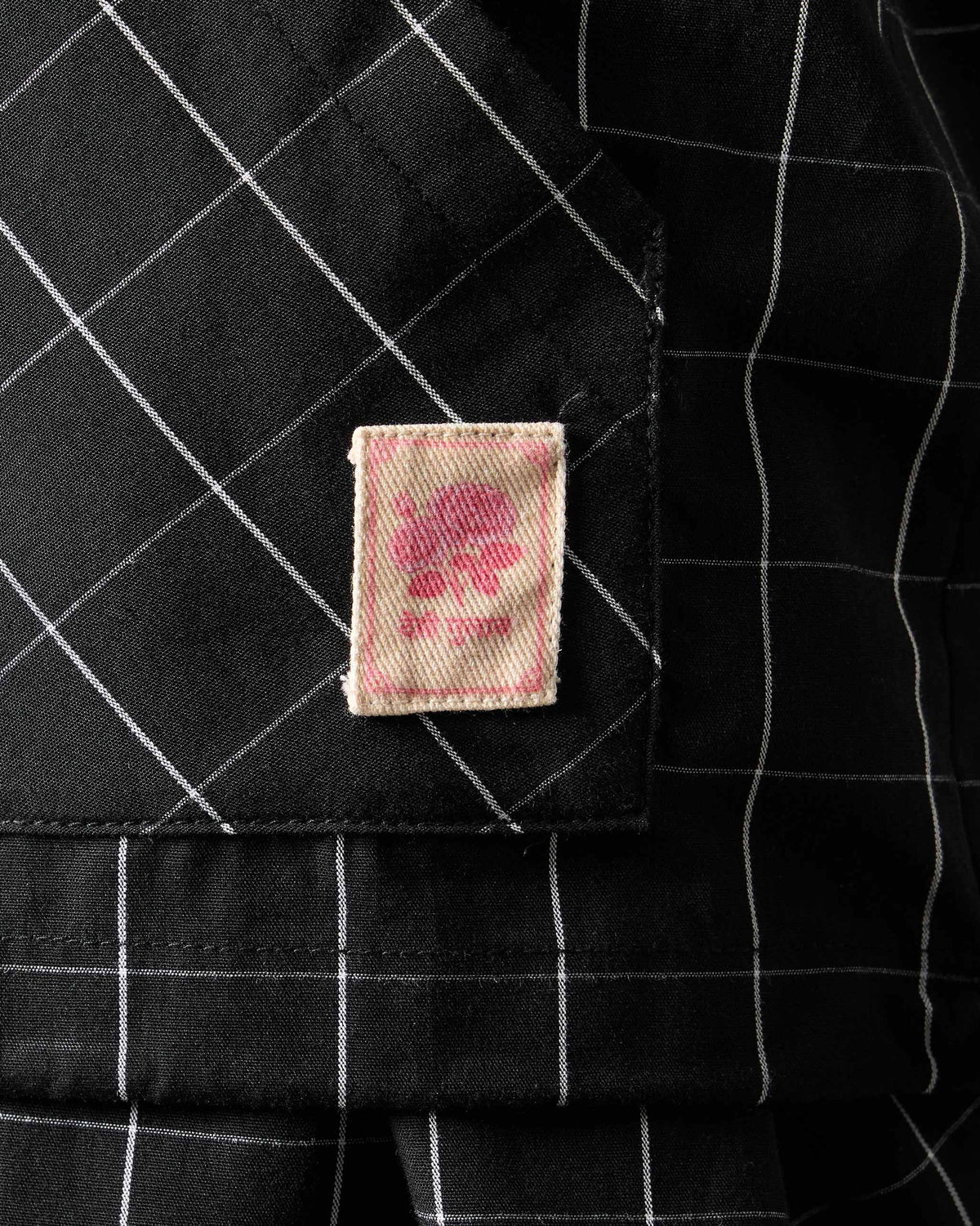 Close-up of a rose label patch on a black-and-white checked Renai top.