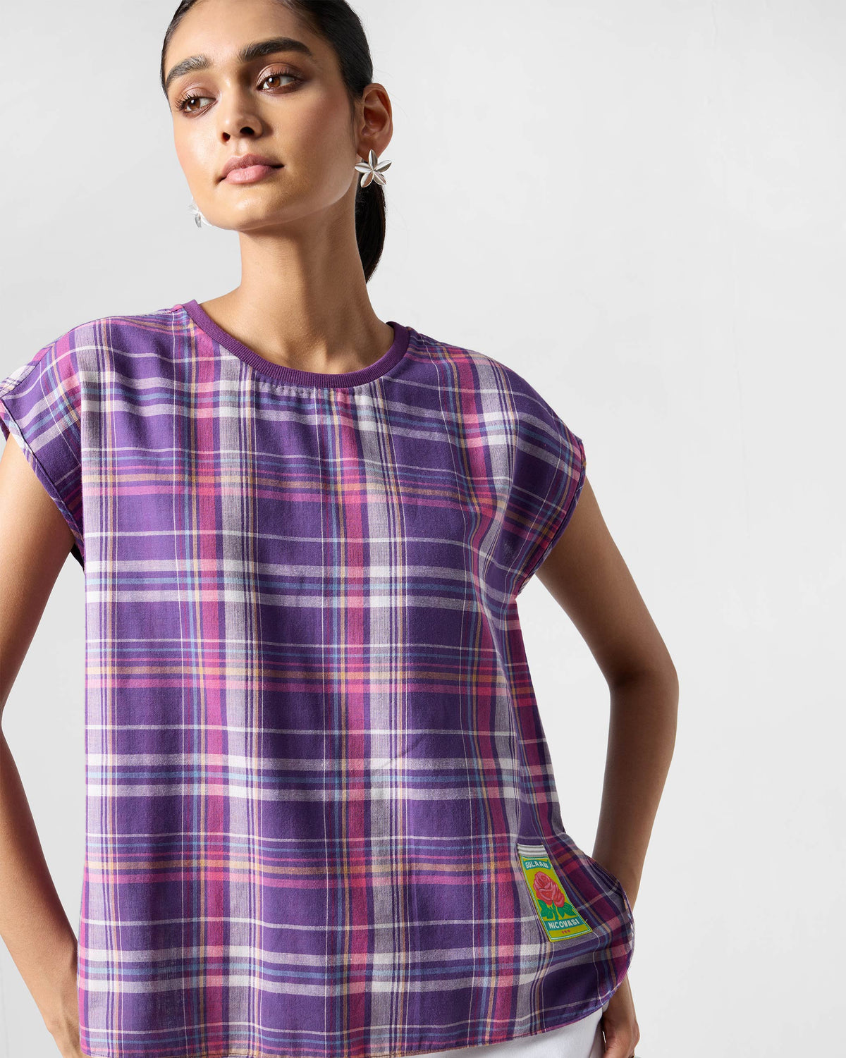 Person wearing a purple plaid Flow top with a crew neck and rose patch.