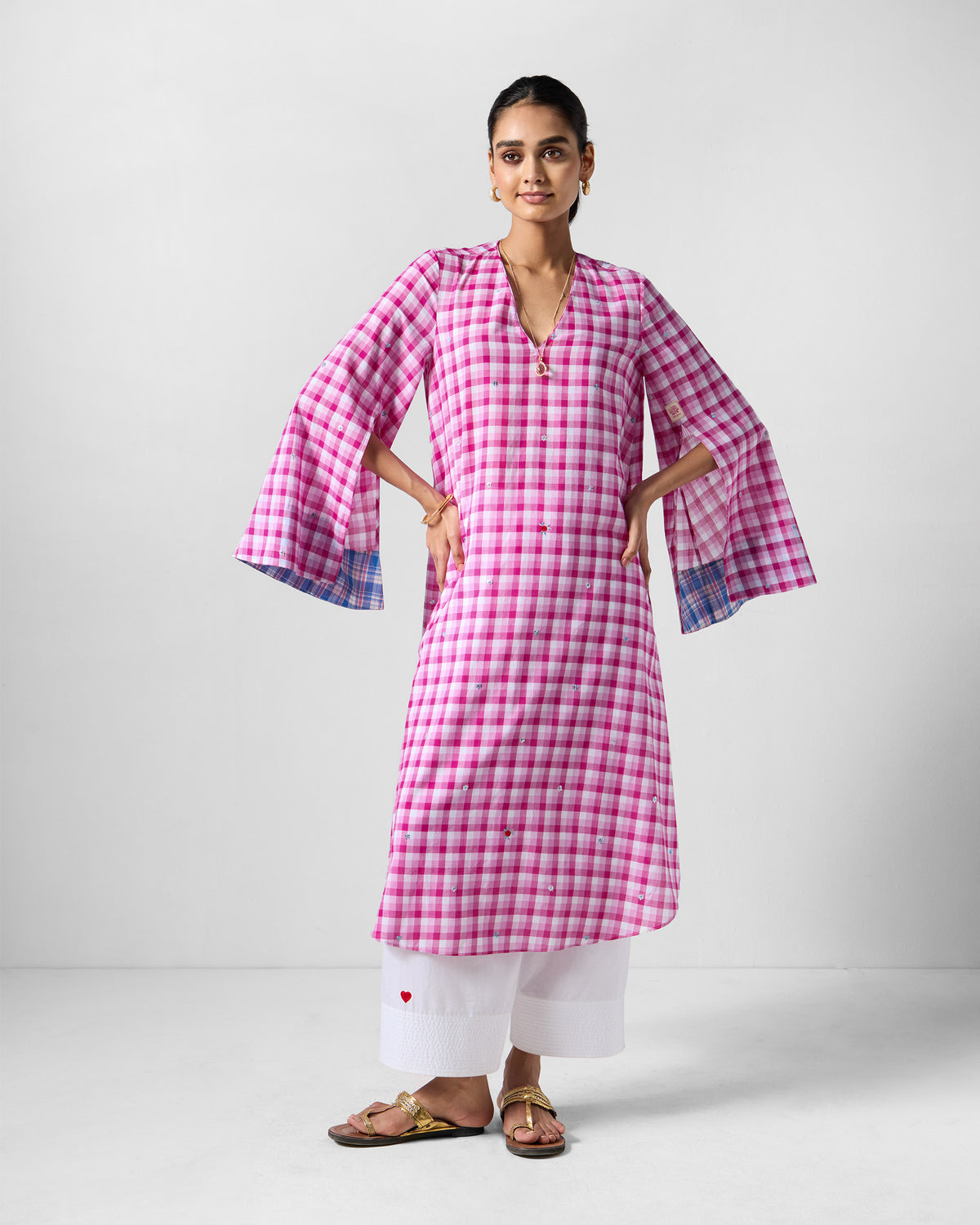 Person wearing a pink and white check embroidered Amaya tunic with slit sleeves.