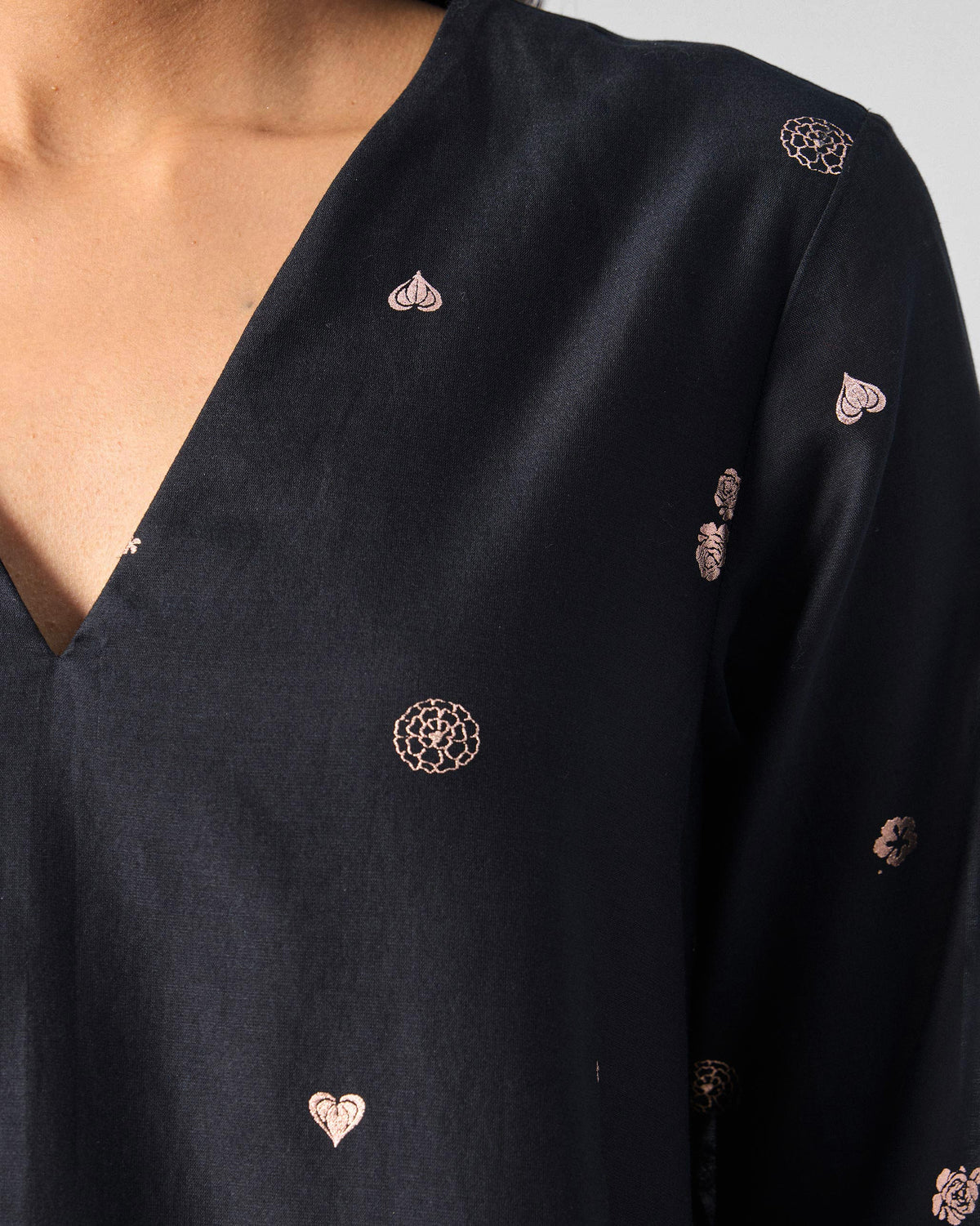 Close-up of pink foil motifs at the V-neck of a black flared dress.