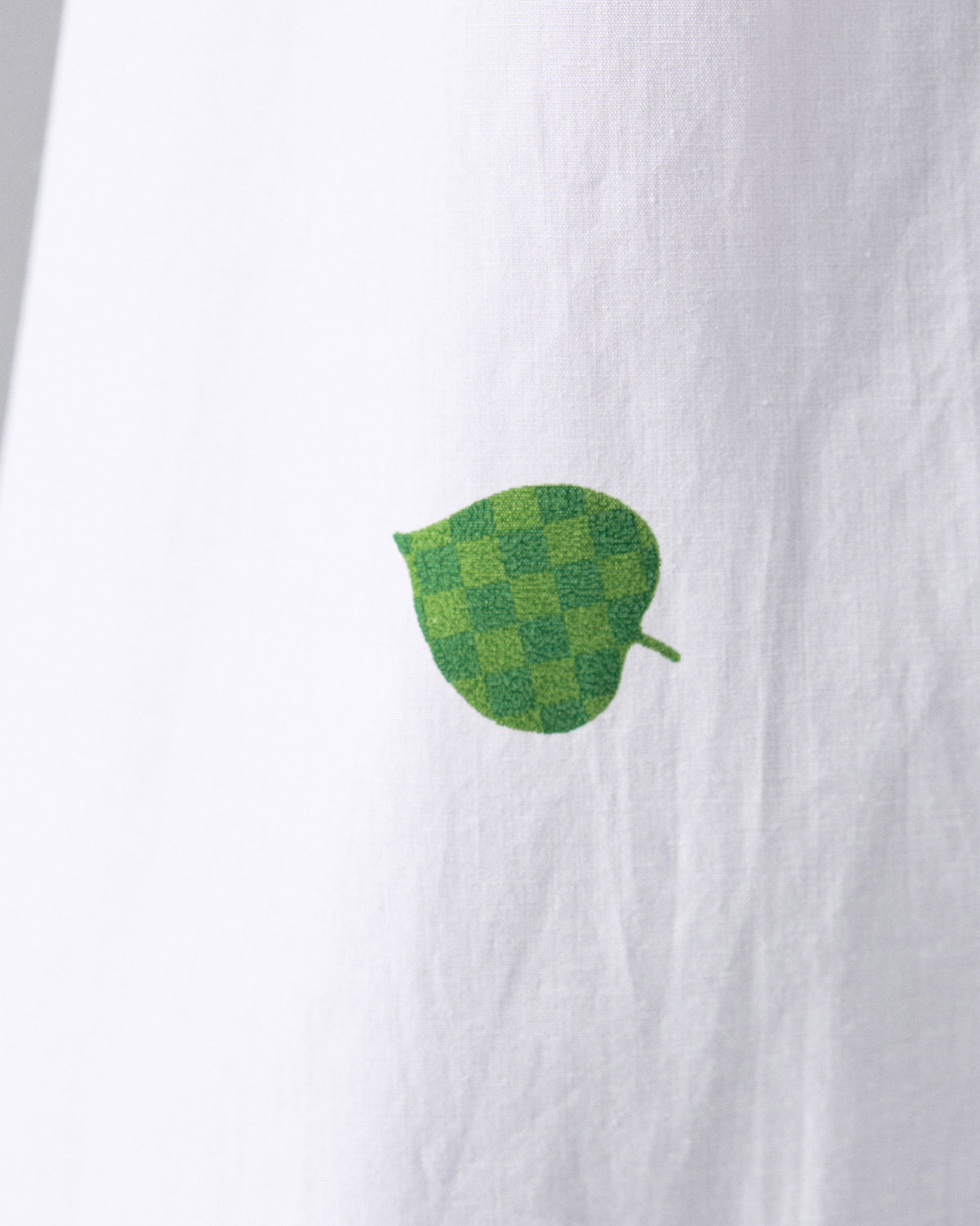 Close-up of a white dress with a small green leaf embroidery.