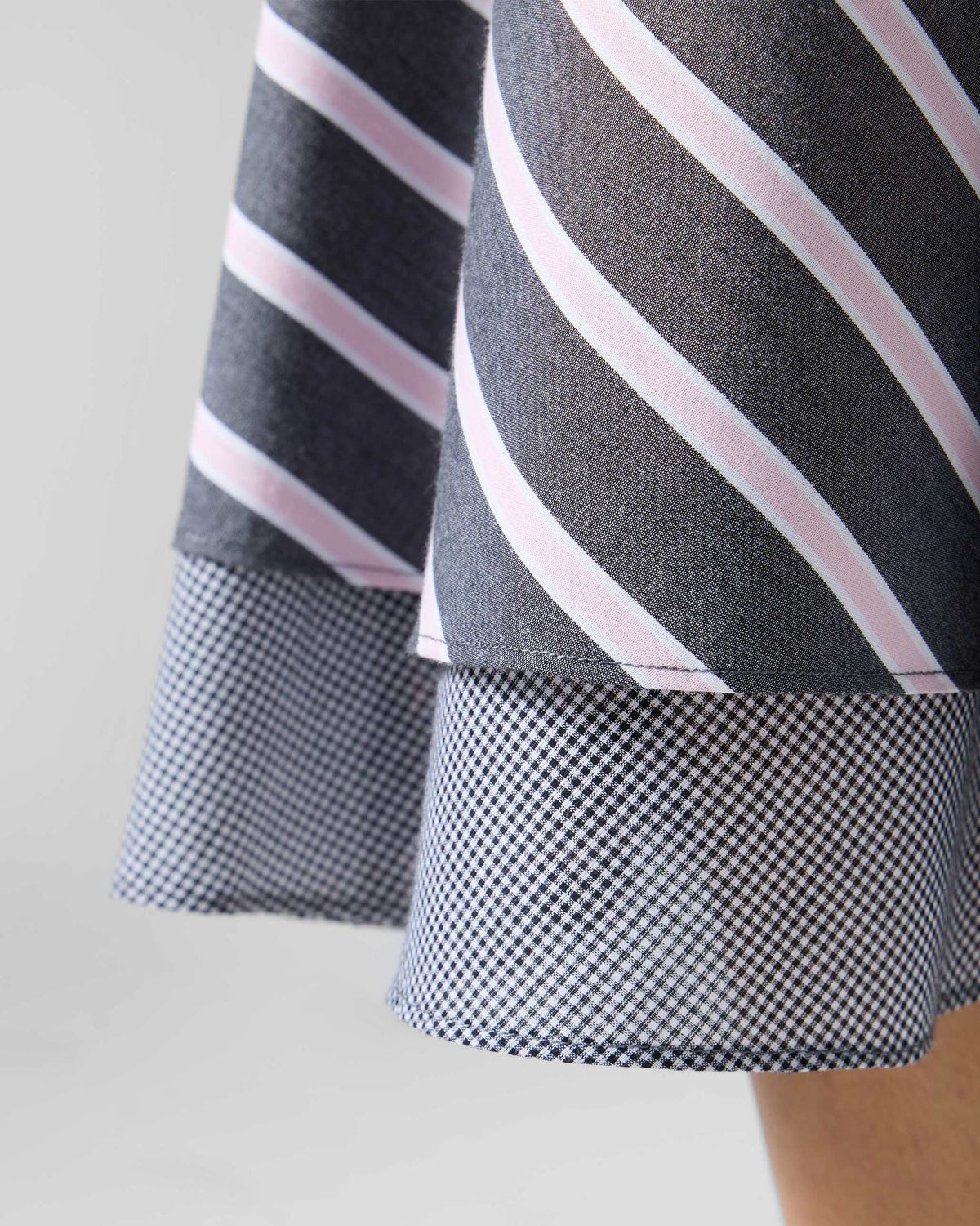 Close-up of a Tapas layered dress showing a striped hem over a check underlayer.