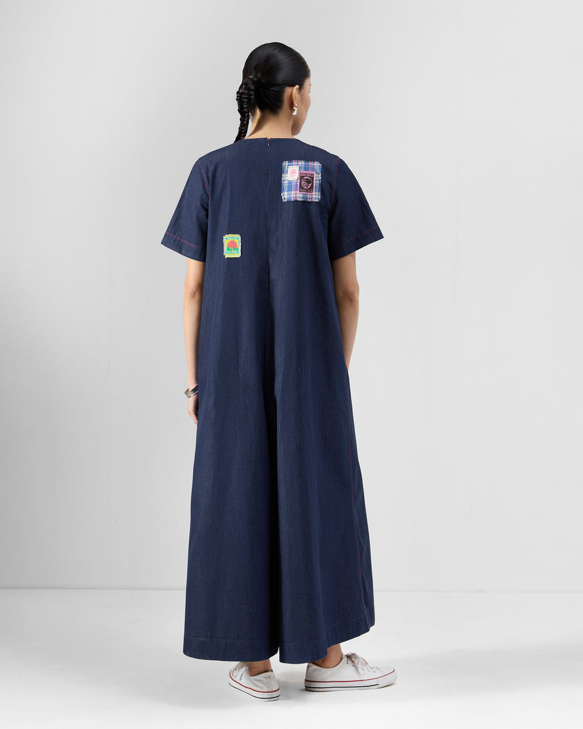 Back of a navy Peru jumpsuit with patches across the upper back, worn by a person.
