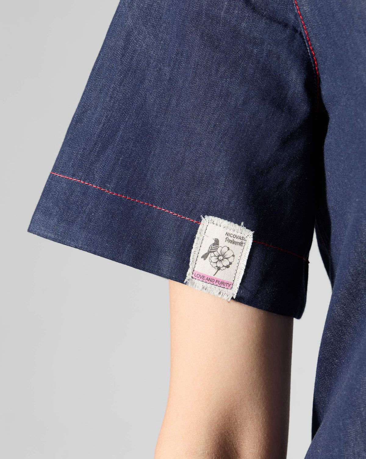 Close-up of a navy Peru jumpsuit sleeve with a small floral Love and Purity label.