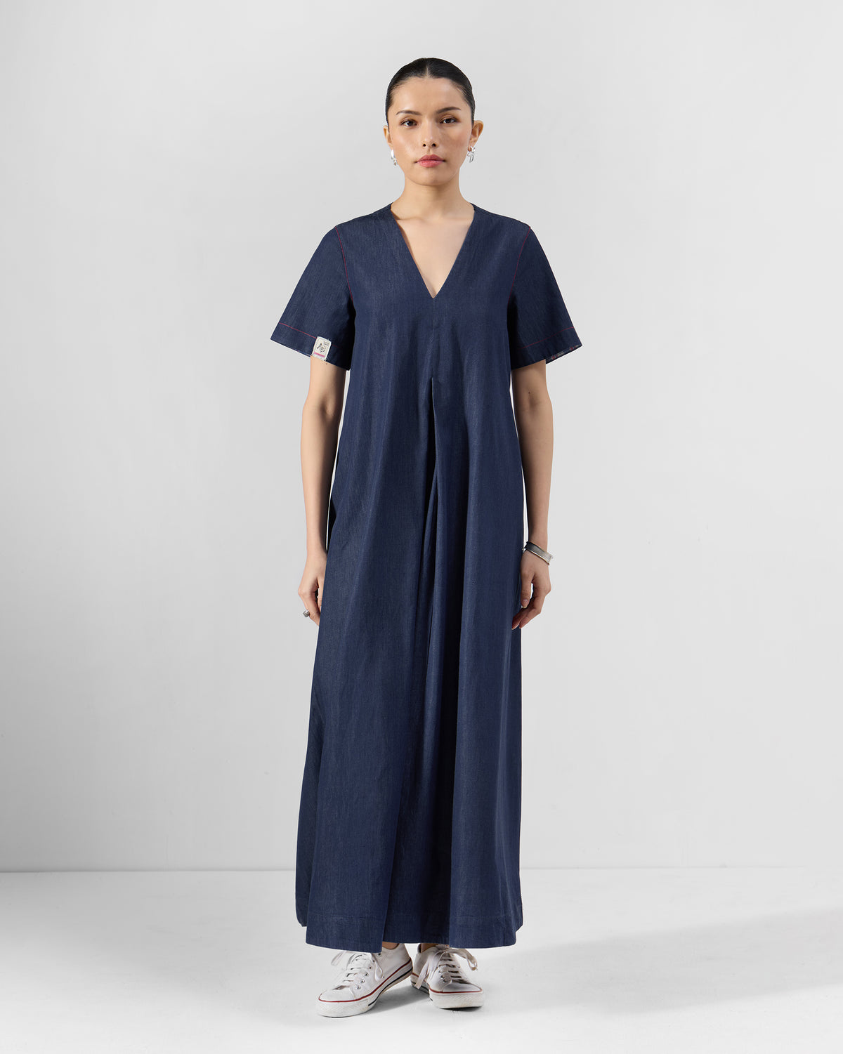 Person standing front-on in a navy Peru jumpsuit with a V-neck and central pleat panel.