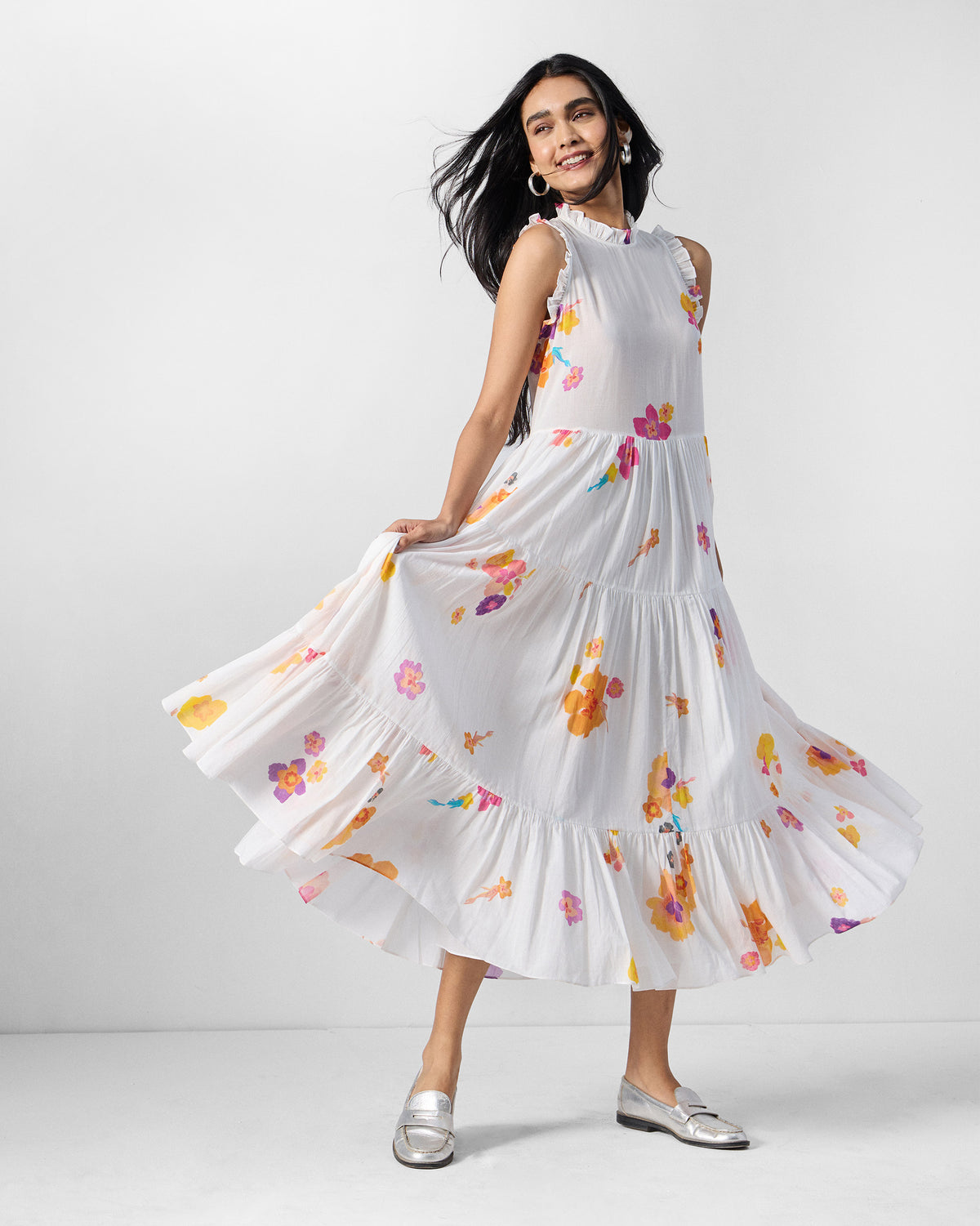 Person holding out the tiered skirt of an ivory floral Reah dress.