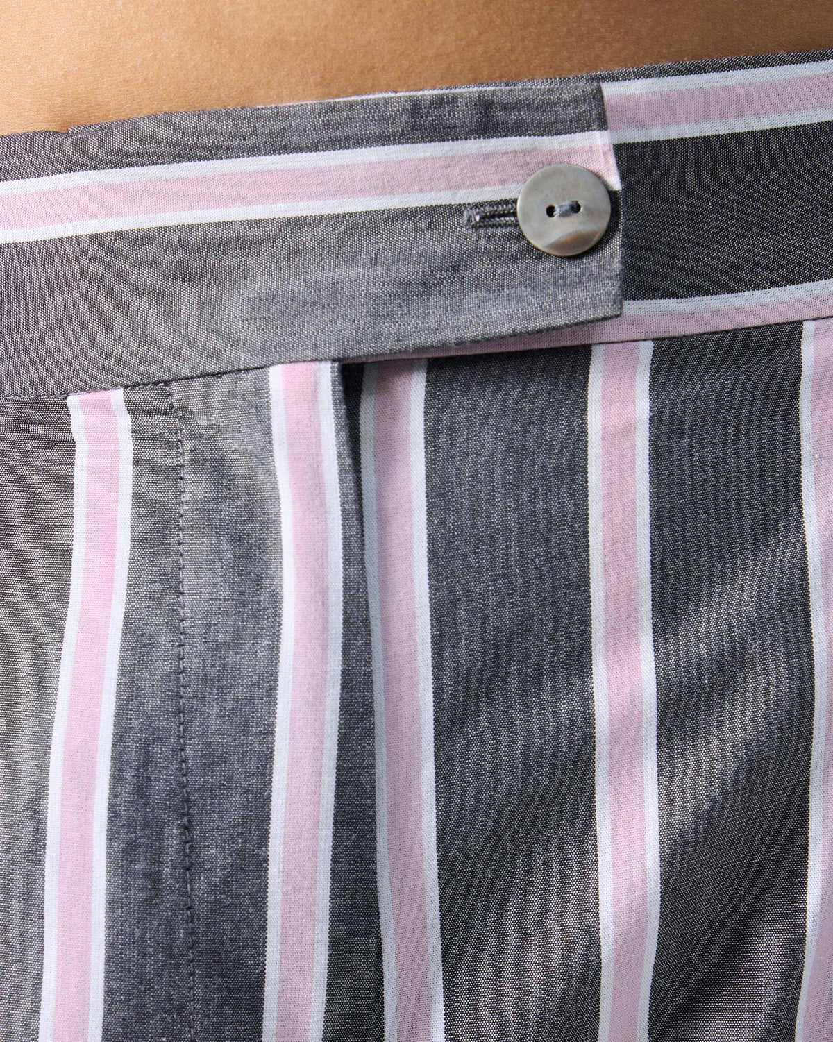 Close-up of the striped waistband and button on charcoal and pink Row pants.