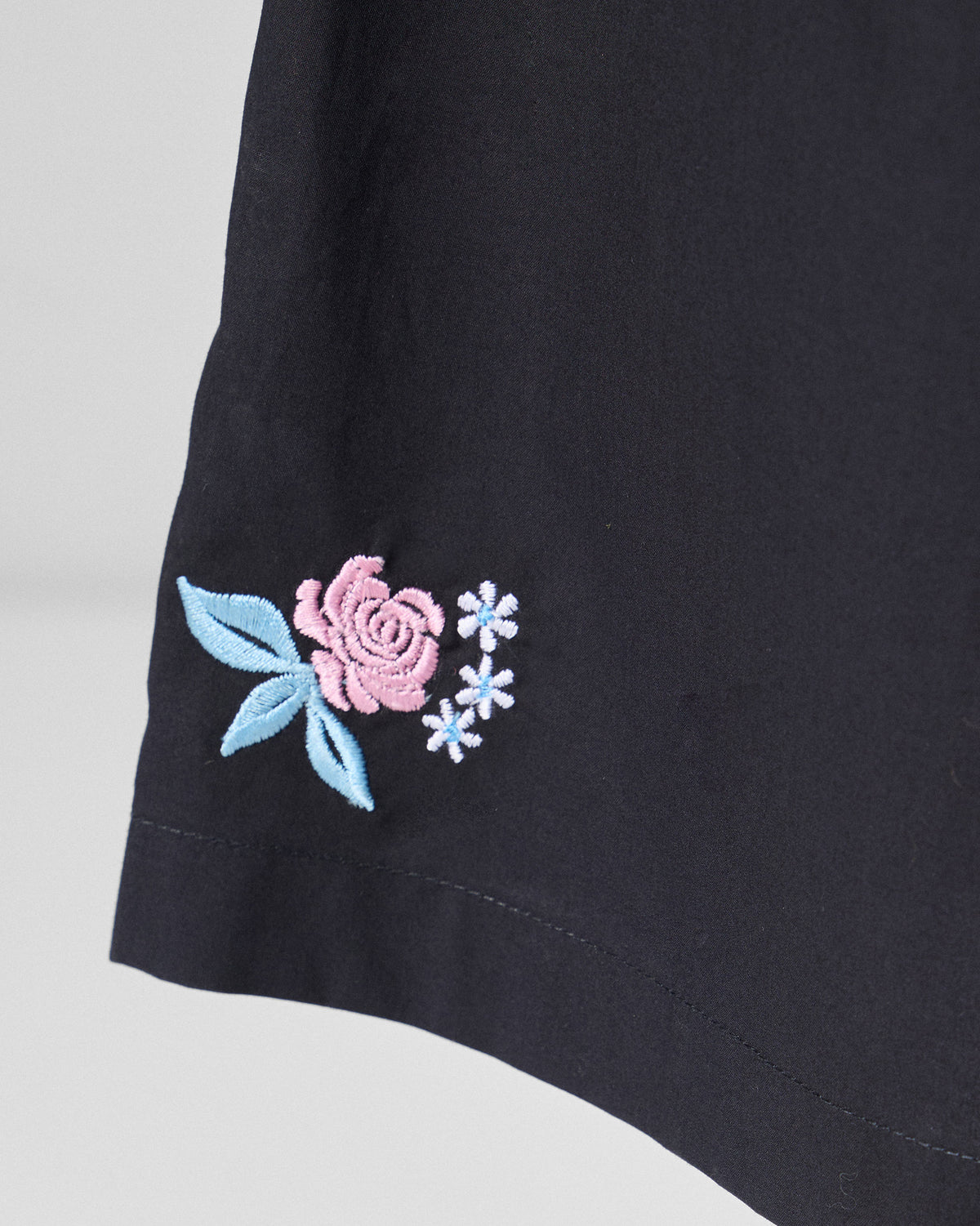 Close-up of a pink rose embroidery on black Bank pants.