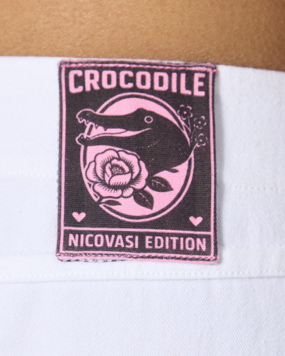 Close-up of the crocodile label on the back waistband of white Ella culottes.