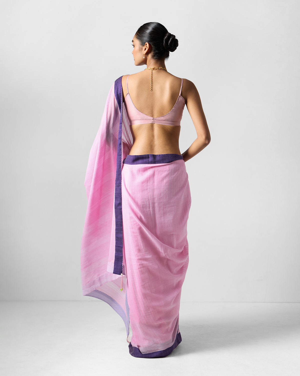 Back of a pink Noor sari with a purple border draped over the shoulder.