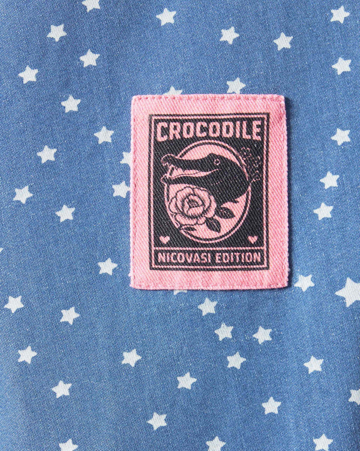 Close-up of a blue star-print dress with a pink crocodile patch.