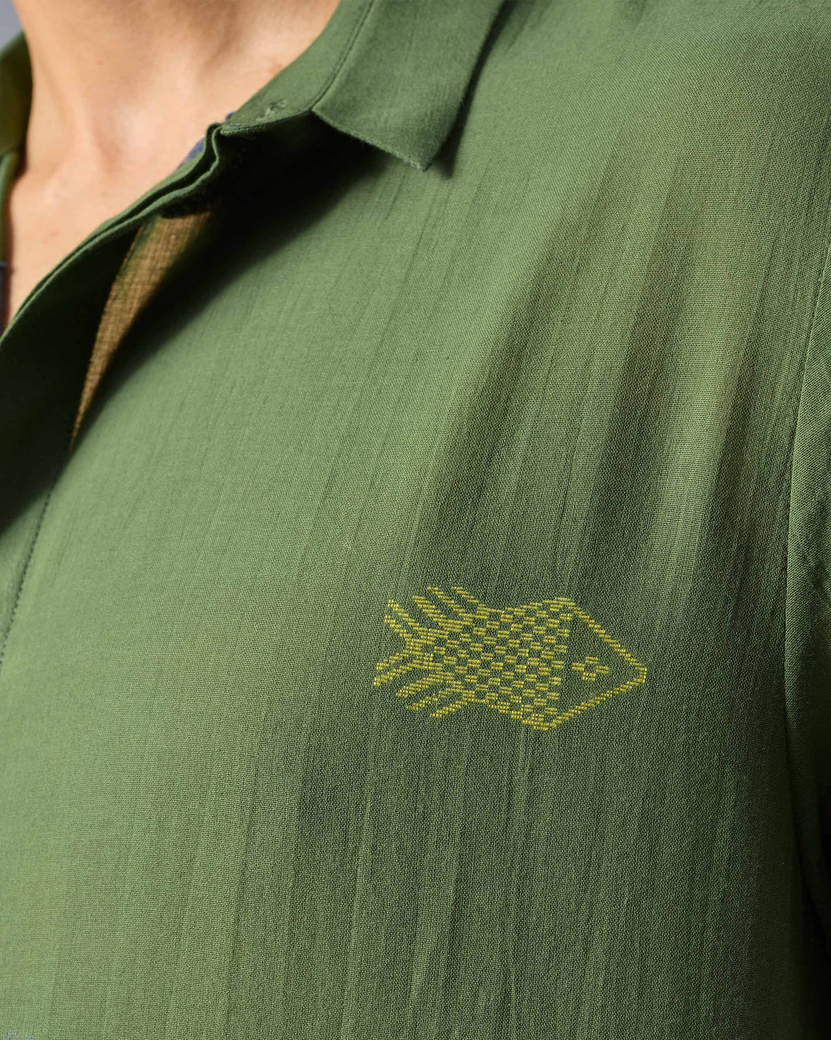 Close-up of a green Riverine shirt with a yellow embroidered fish.