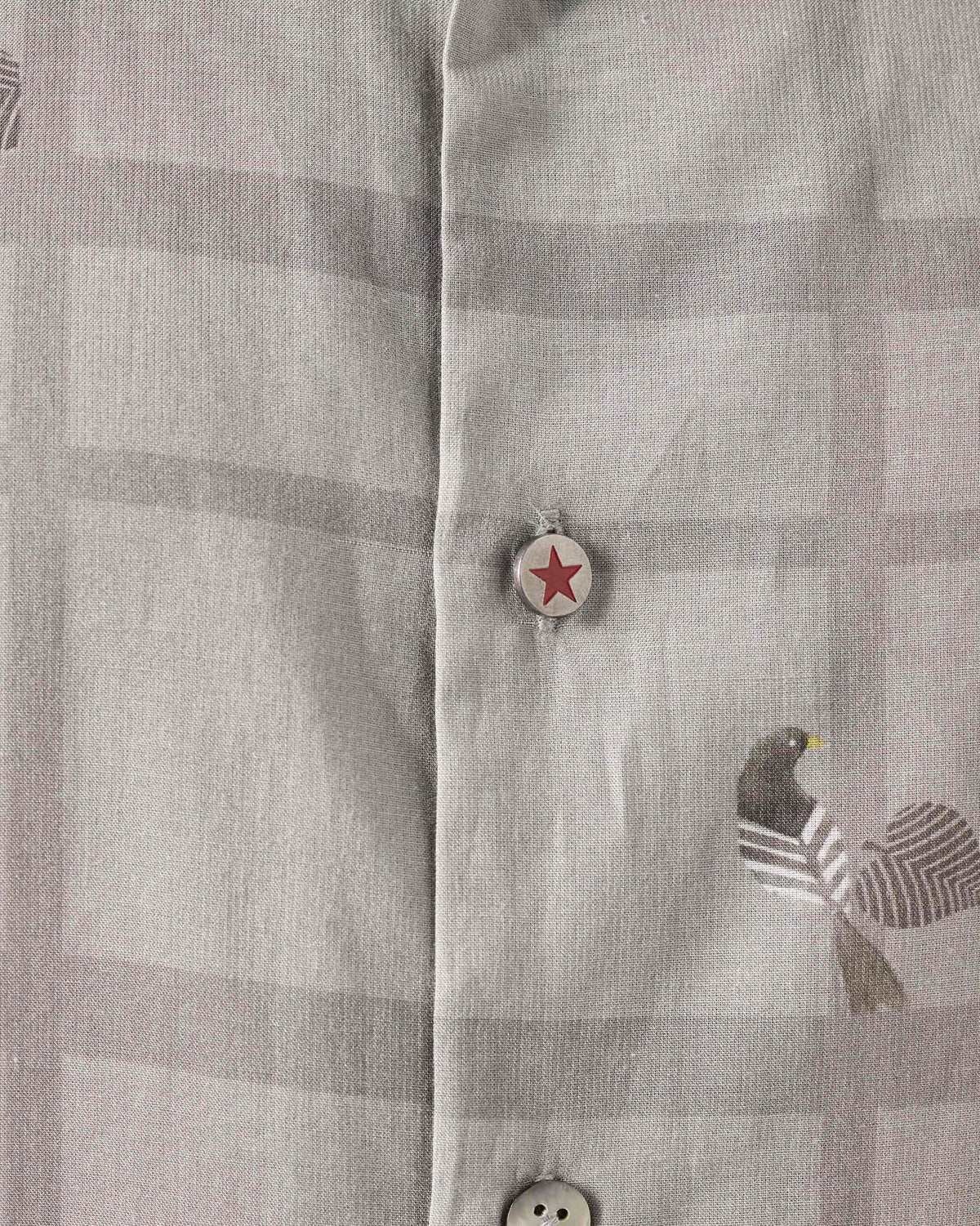 Close-up of a charcoal Mistari Shirt showing a bird print and red star button.