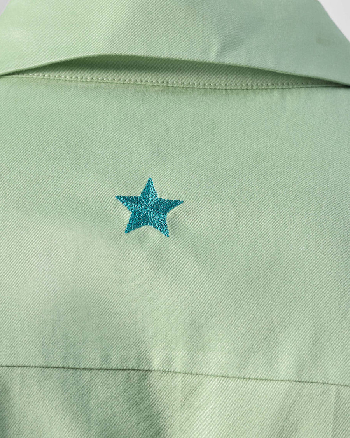 Close-up of a teal embroidered star on the sage green Jaisal Shirt yoke.
