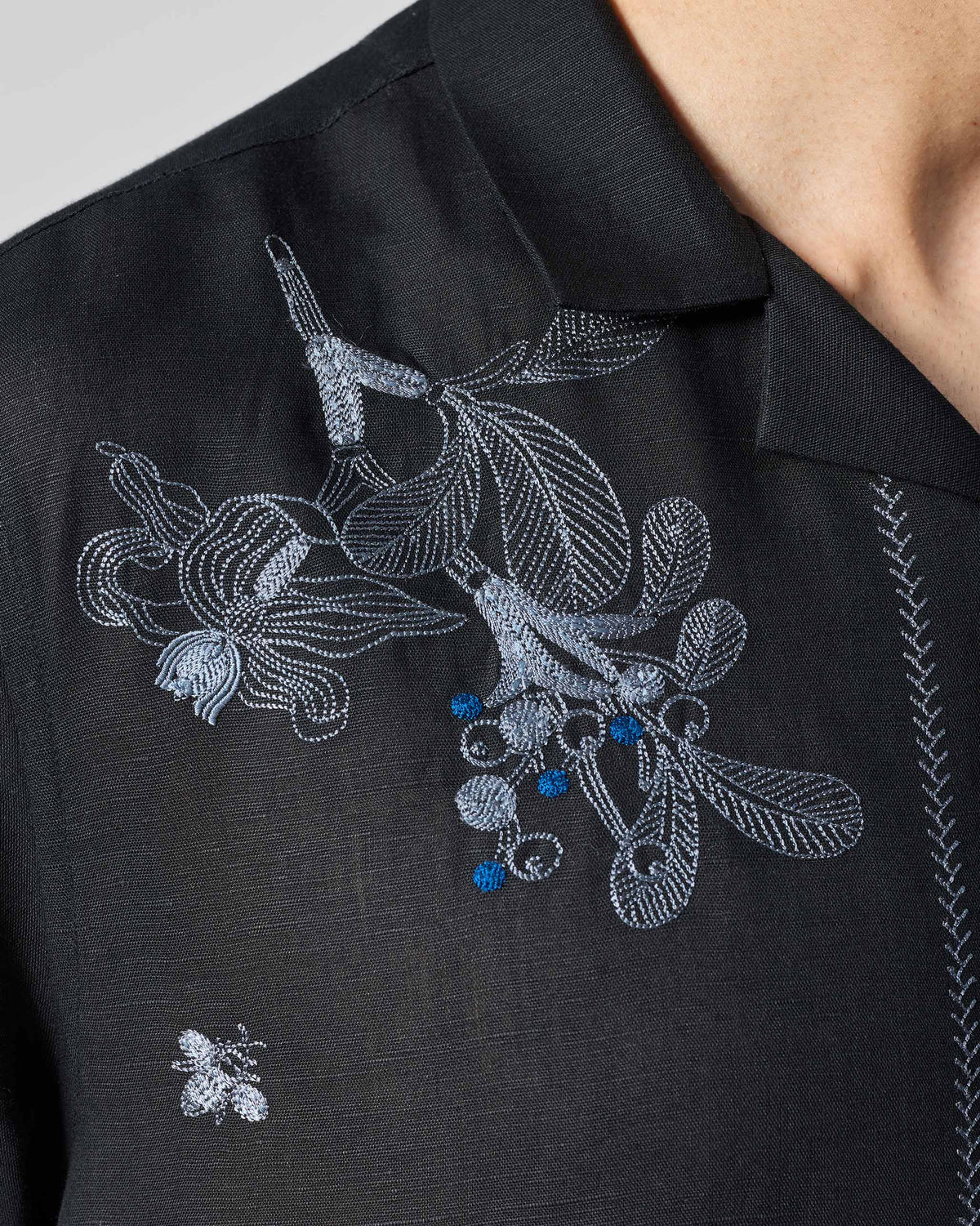 Close-up of blue botanical embroidery on a black Delta shirt.
