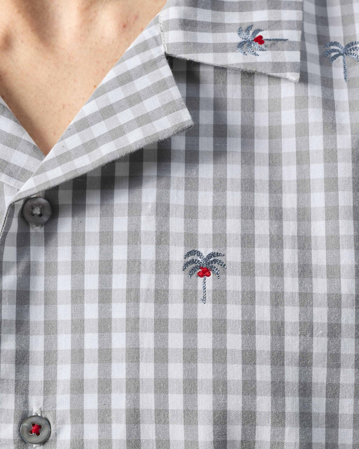 Close-up of a Bena shirt showing palm tree embroidery and a red-stitched placket button.