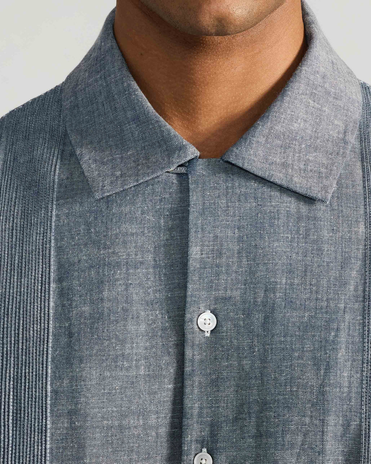 Close-up of an indigo shirt chest with white buttons and fine pintuck panels beside the placket.