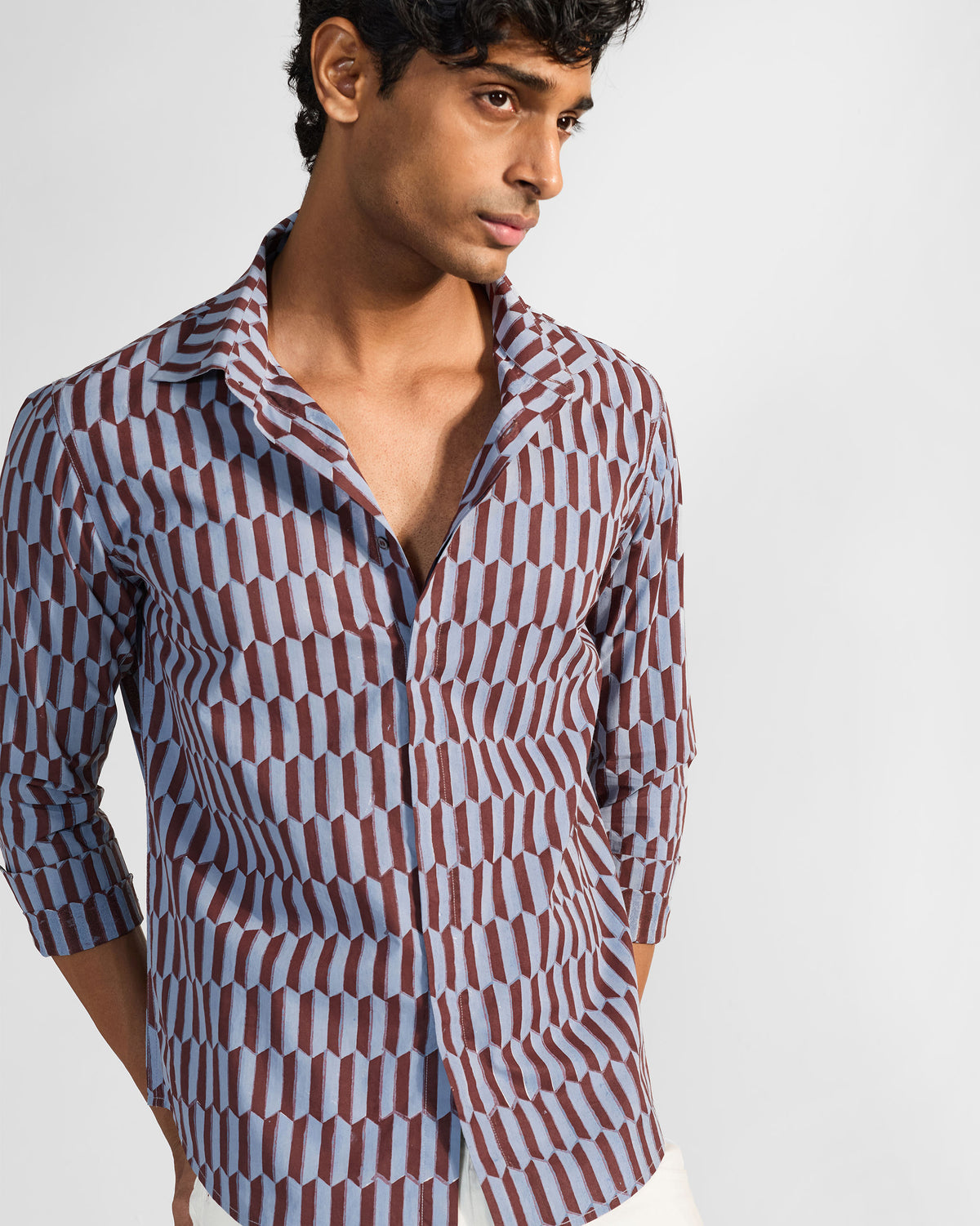 Person wearing a brown and light blue geometric print Drongo shirt with an open collar.