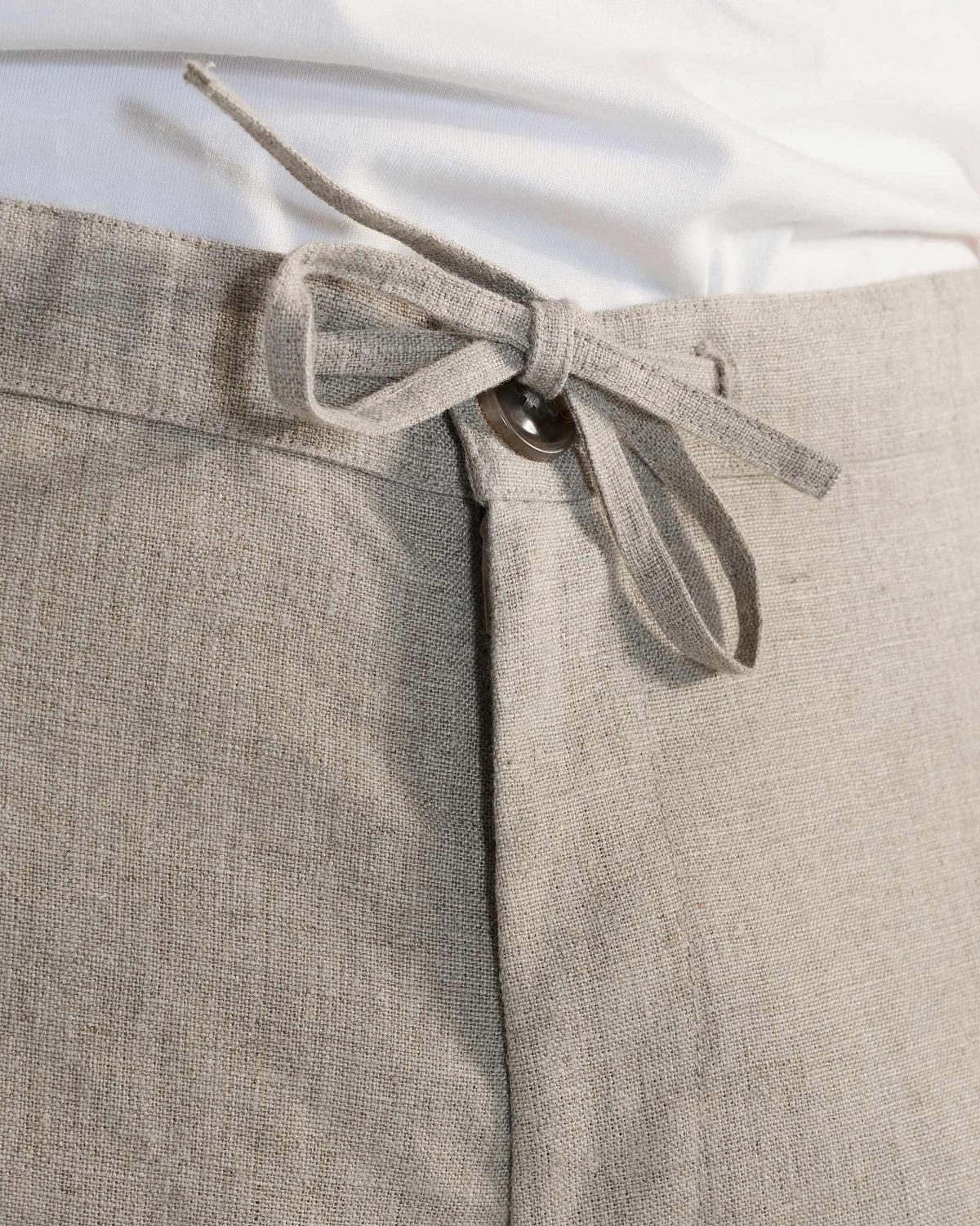Close-up of beige Ibex Trousers showing the drawstring waistband and button fly.
