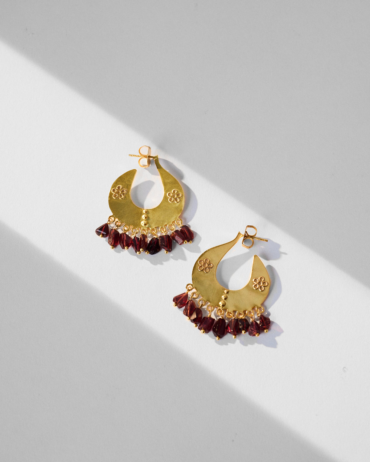 Pair of gold Anaar crescent earrings with red glass bead fringes laid flat.