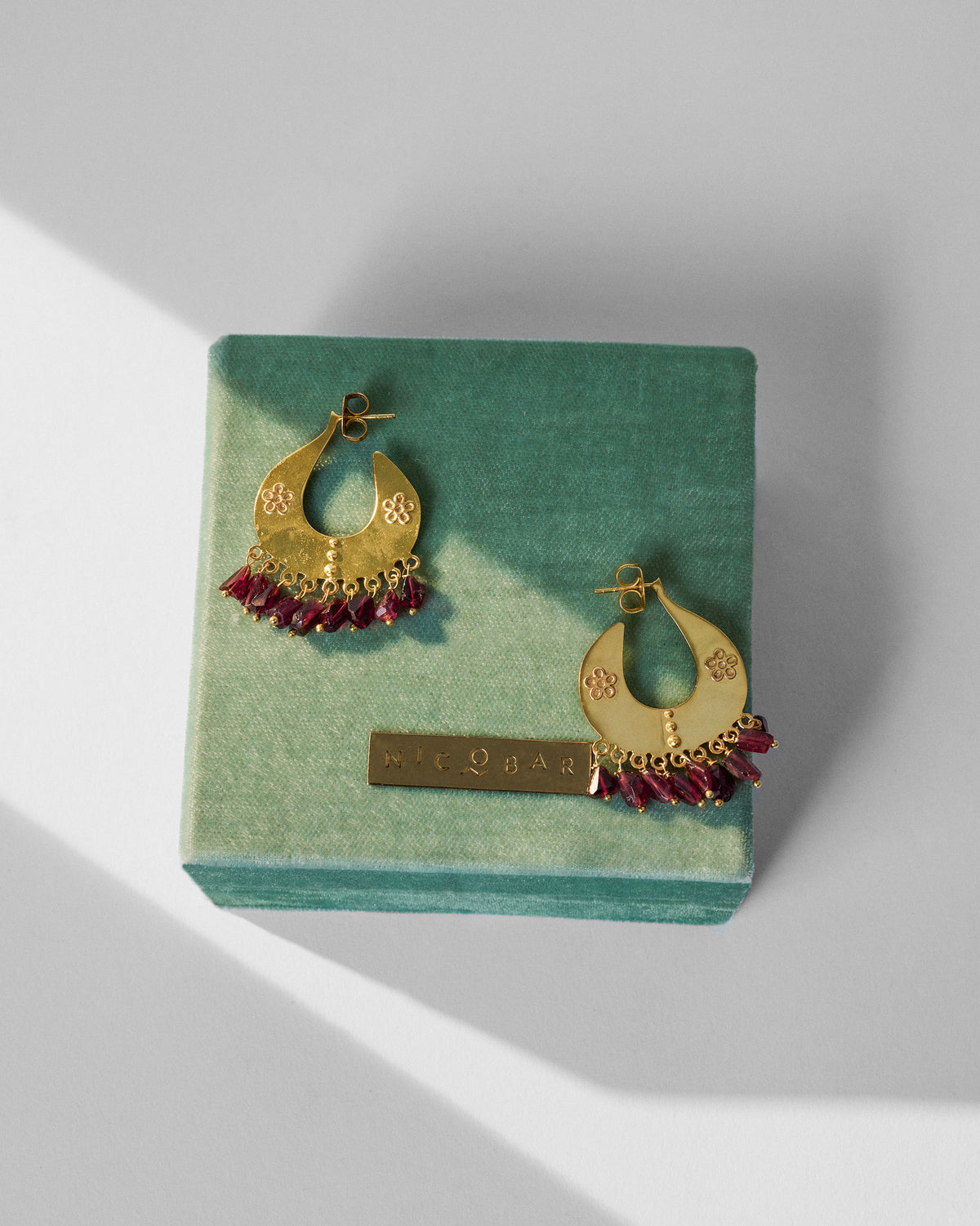 Gold Anaar earrings with red bead fringes on a green Nicobar gift box.