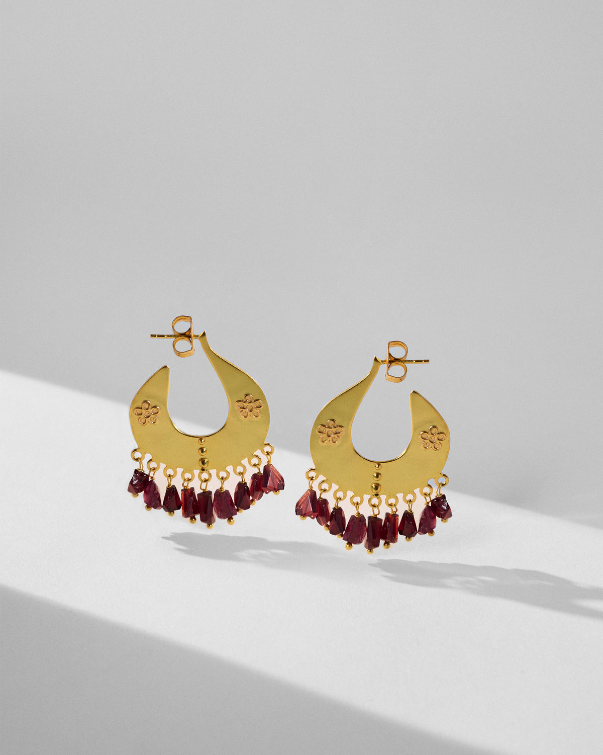 Pair of gold Anaar crescent earrings with dark red glass drop fringes.