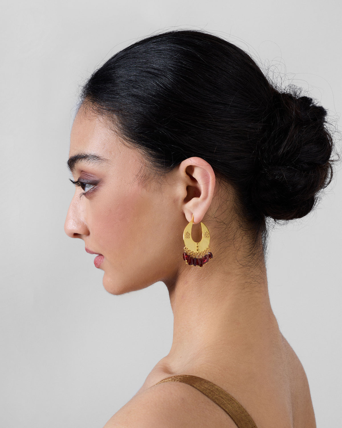 Side profile of a gold Anaar crescent earring with red beads on a person.