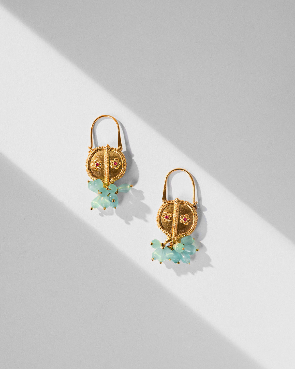 Pair of gold Anaar balis with floral red stones and mint bead drops laid flat.