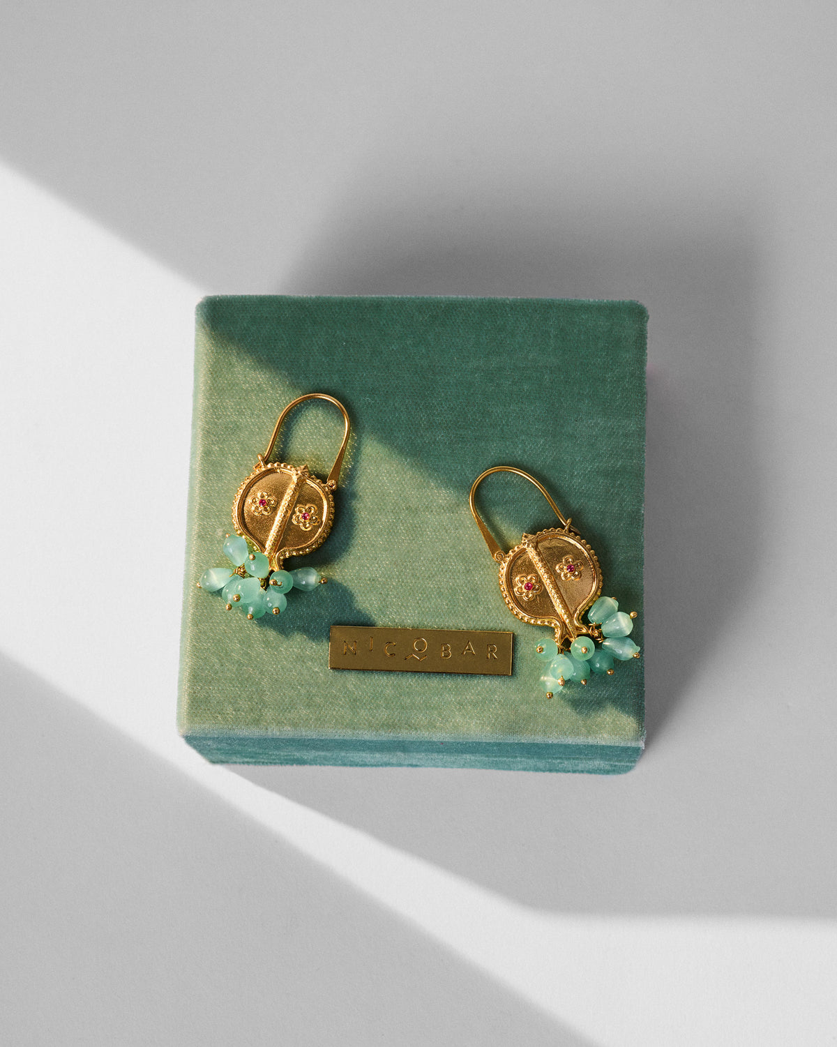Gold Anaar balis with floral stones on a green Nicobar gift box.