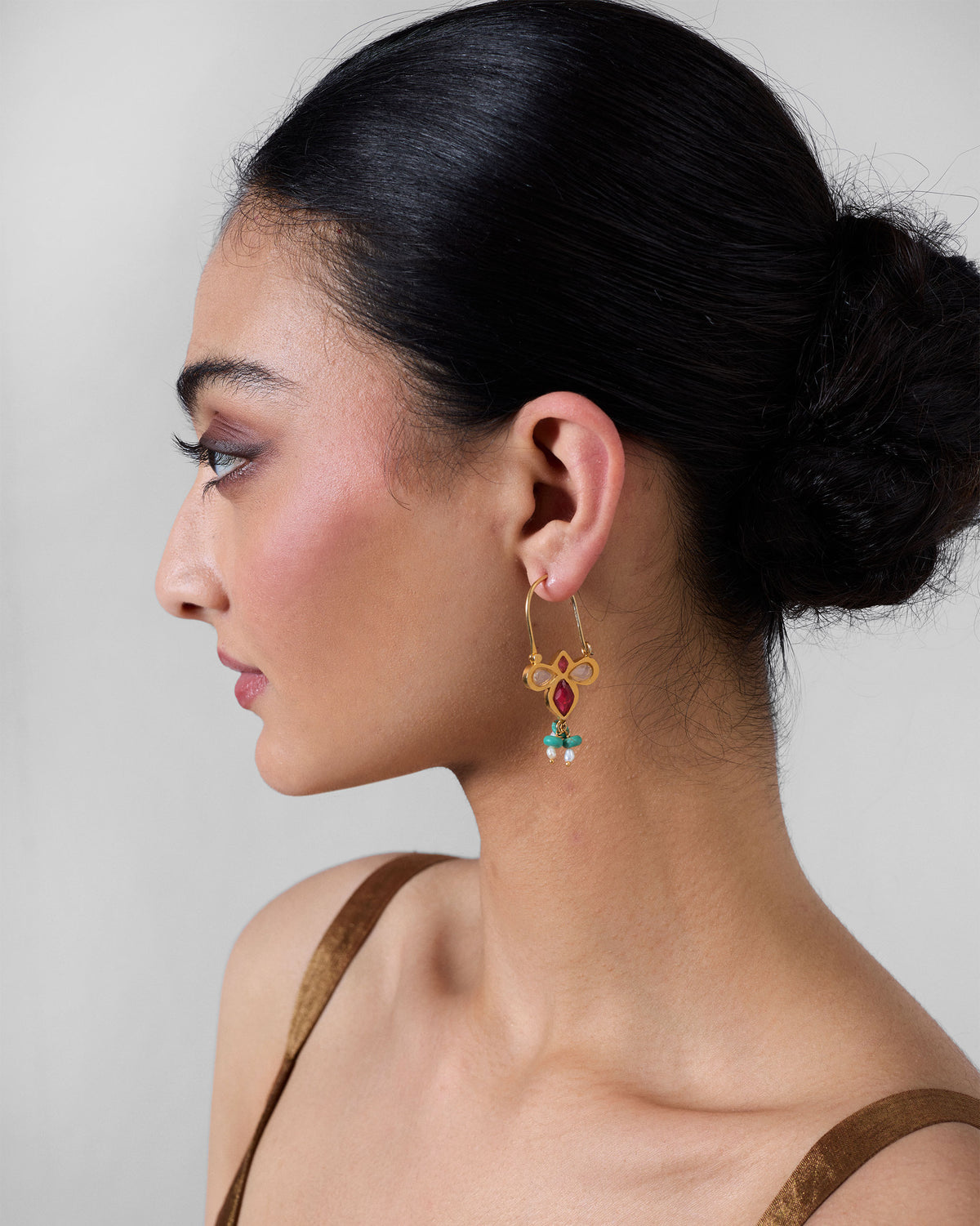 Person wearing a gold doli earring with pink glass and turquoise tassels.