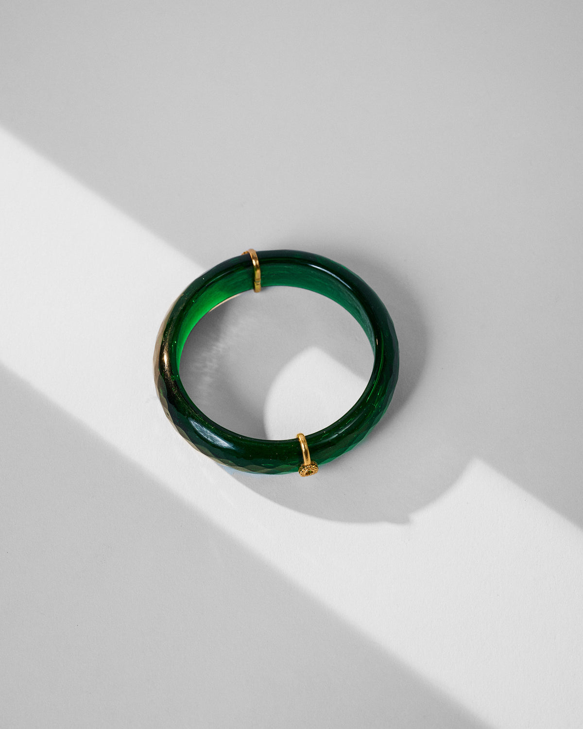 Translucent green glass dhoop bangle with gold bands laid flat.