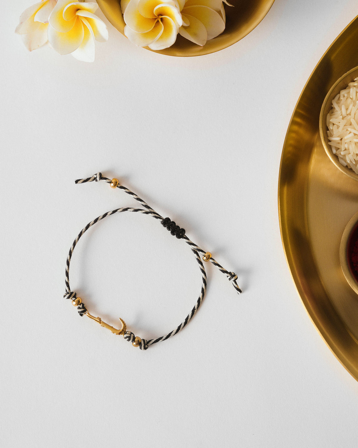 Croc Rakhi laid flat on white, with a gold curved charm and black and white cord.