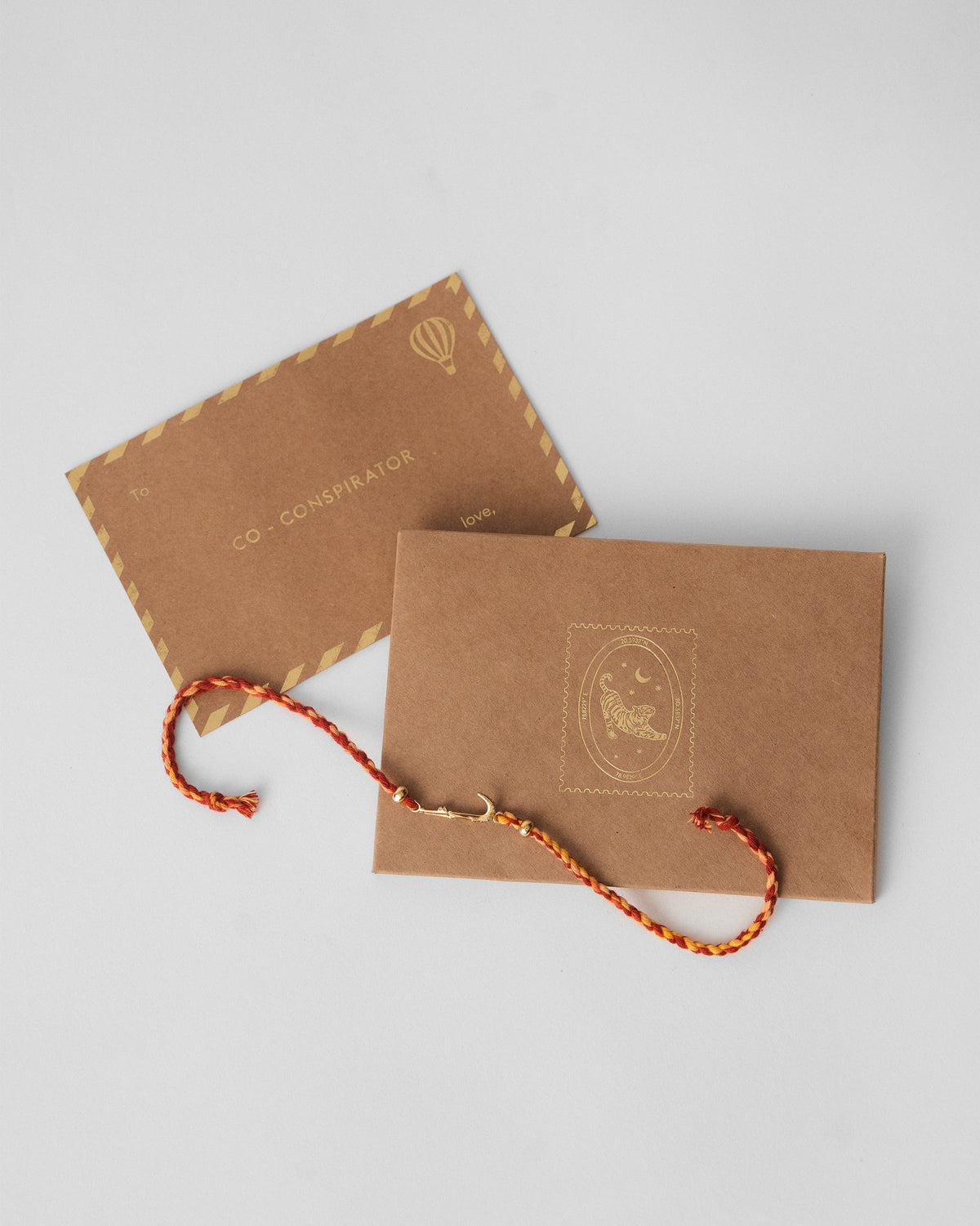 Red Croc Rakhi beside a kraft gift envelope and card.
