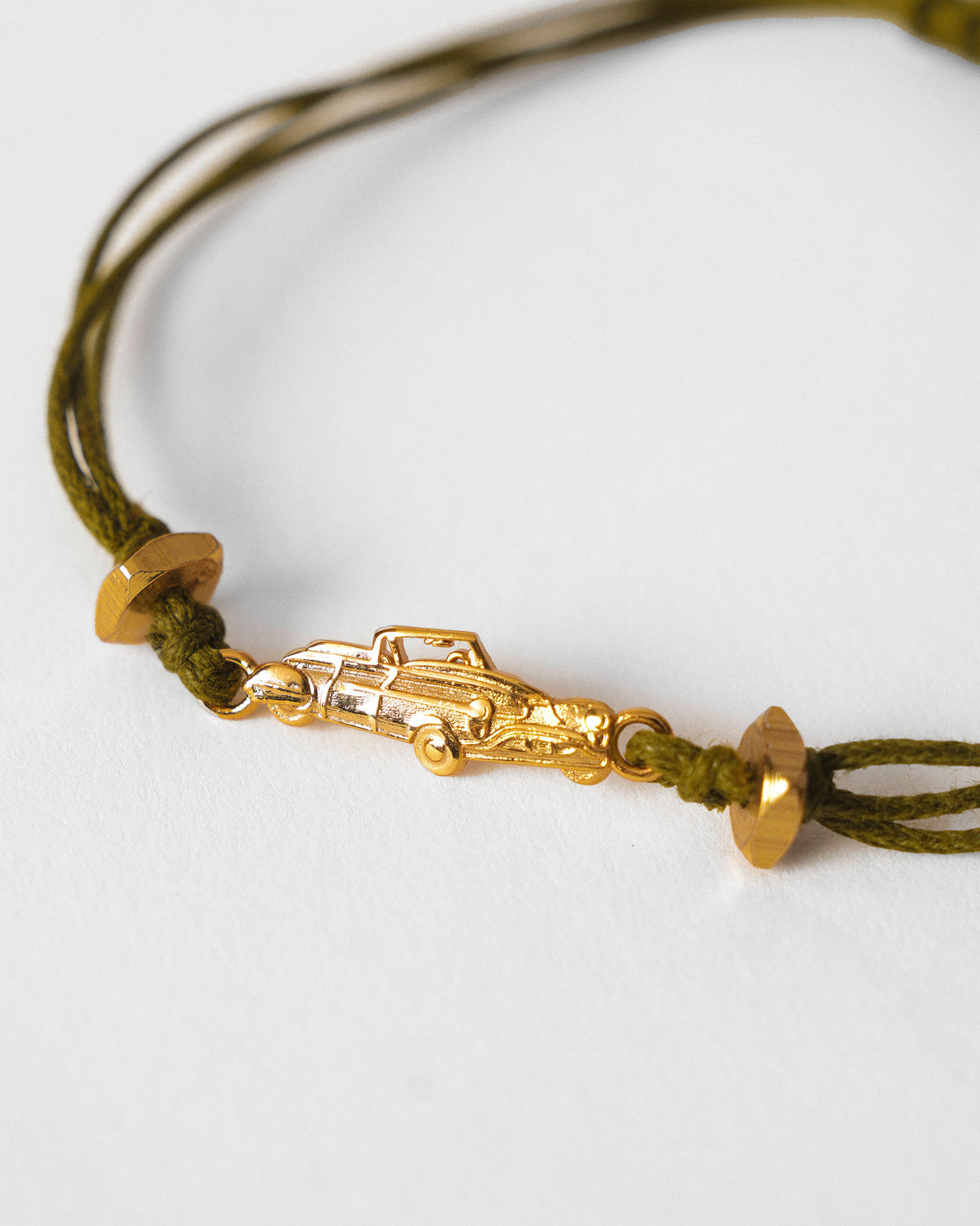 Close-up of a gold car charm on a green cord with gold beads.
