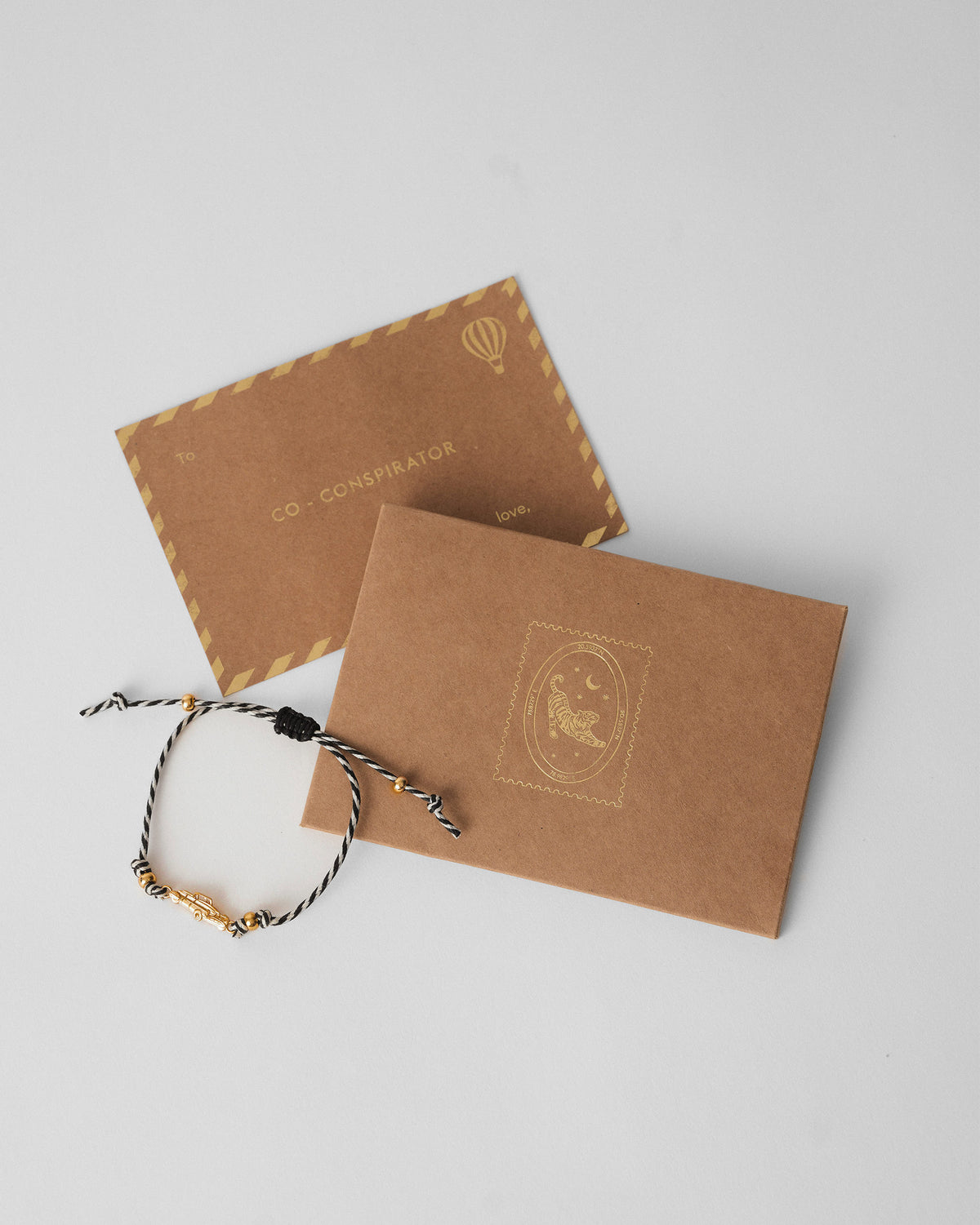 Vintage Car Rakhi in charcoal and white stripes beside kraft gift envelopes.