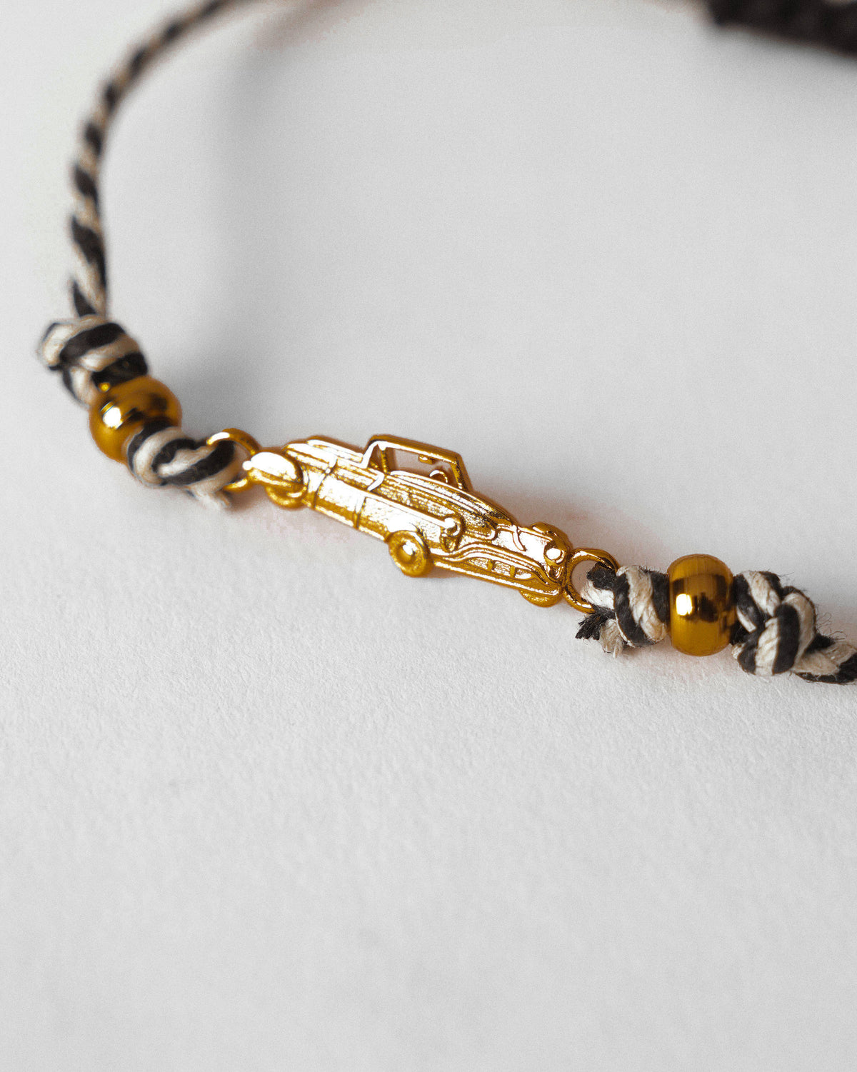 Close-up of a gold car charm on a charcoal and white striped cord with gold beads.