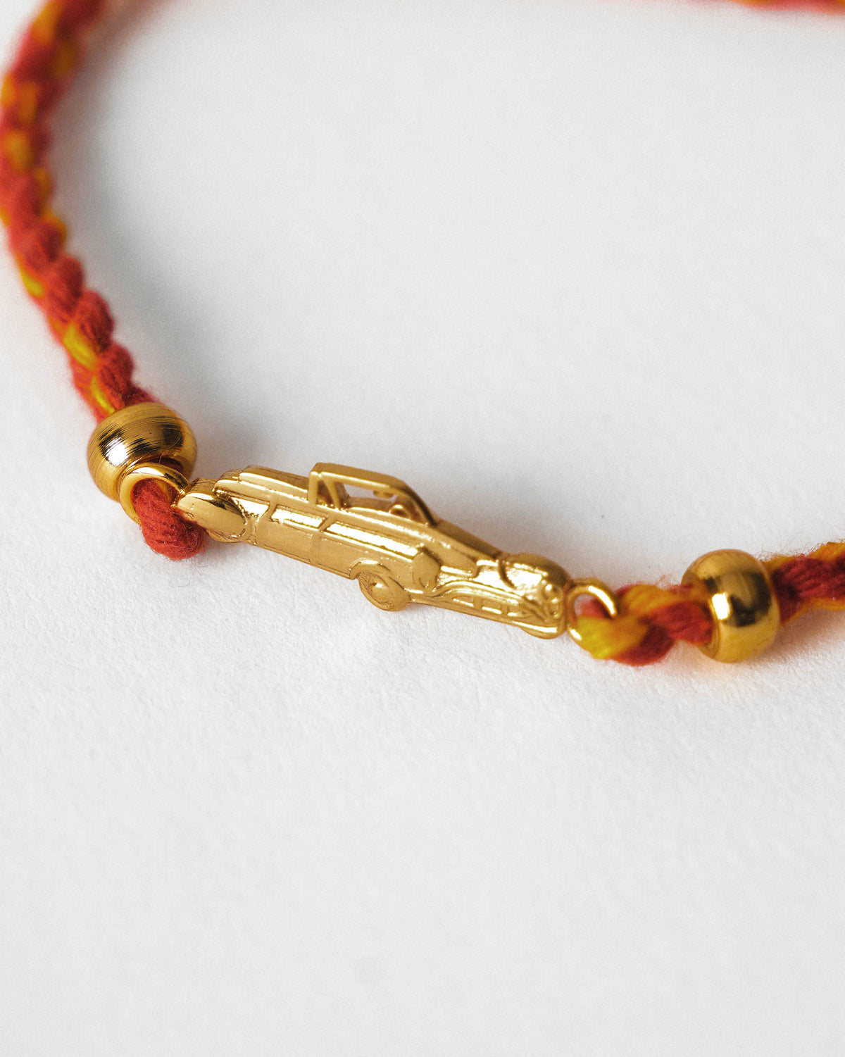 Close-up of a gold car charm on a red and yellow braided cord with gold beads.